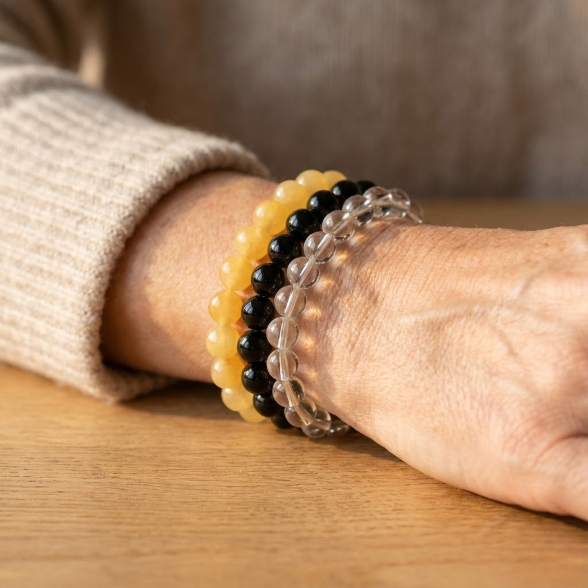 Close-up of a wrist wearing three beaded Abundance intention bracelet stack featuring yellow aventurine, black onyx, and motto glass beads for prosperity and positivity bracelets on a wooden surface.
