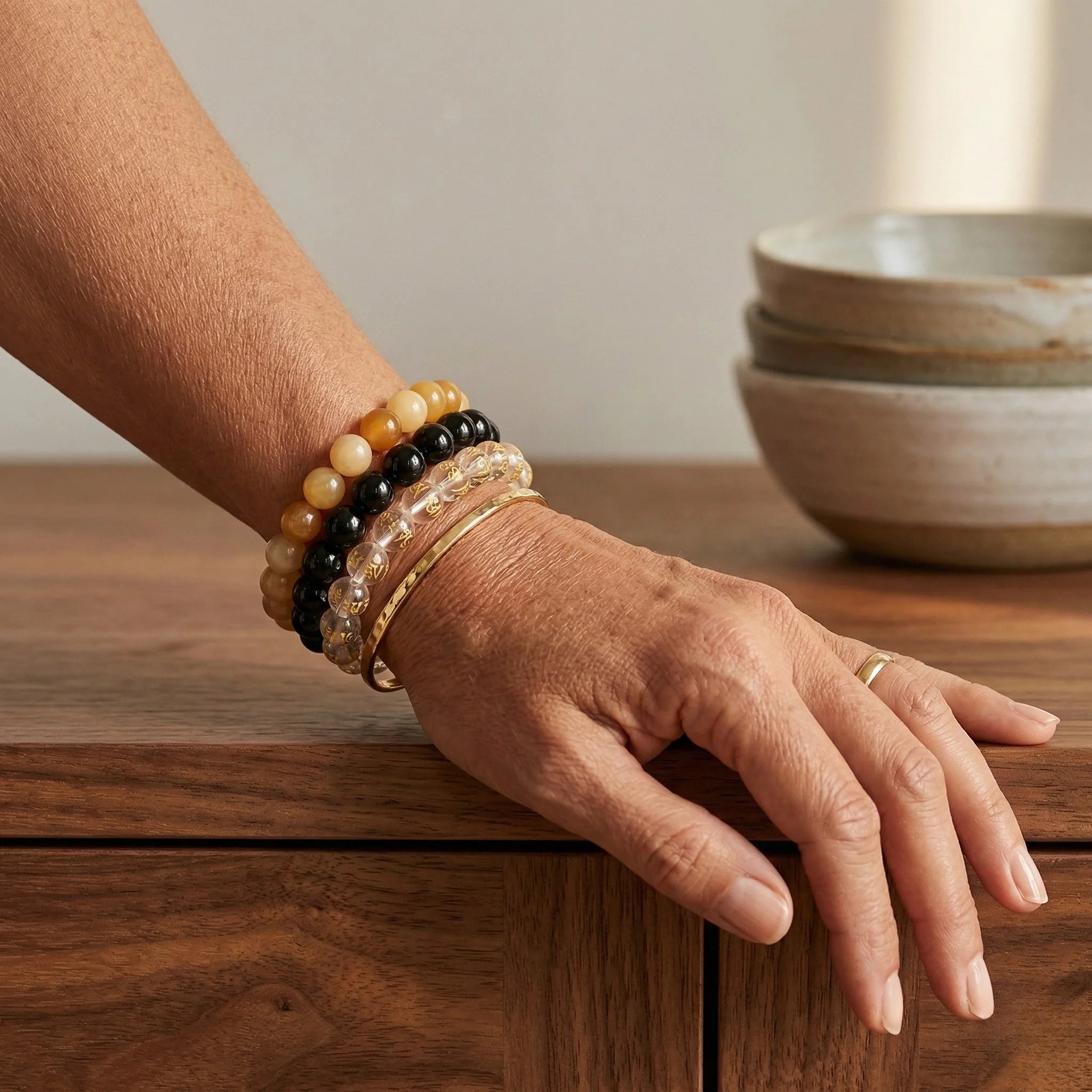 Hand wearing multiple bracelets on a wooden surface with bowls in the background