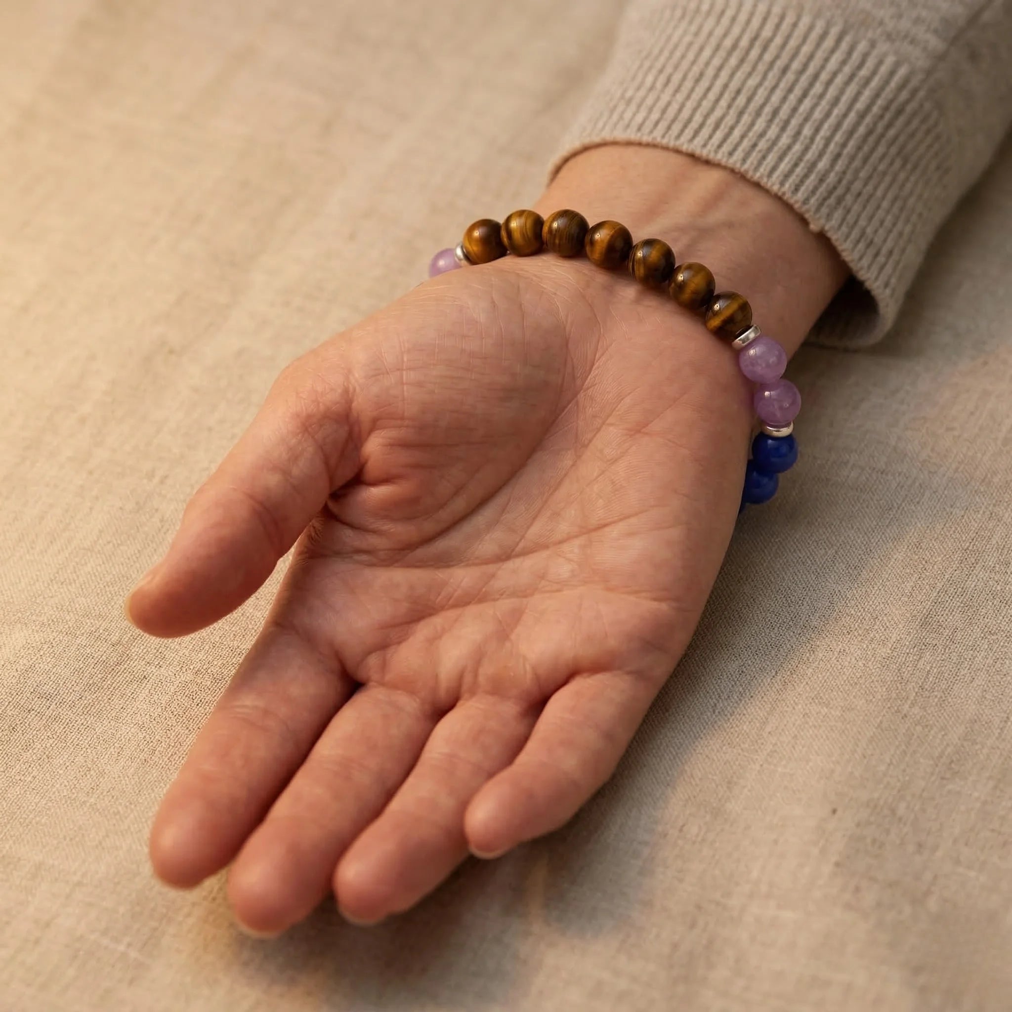 Hand wearing a beaded bracelet on a beige fabric background