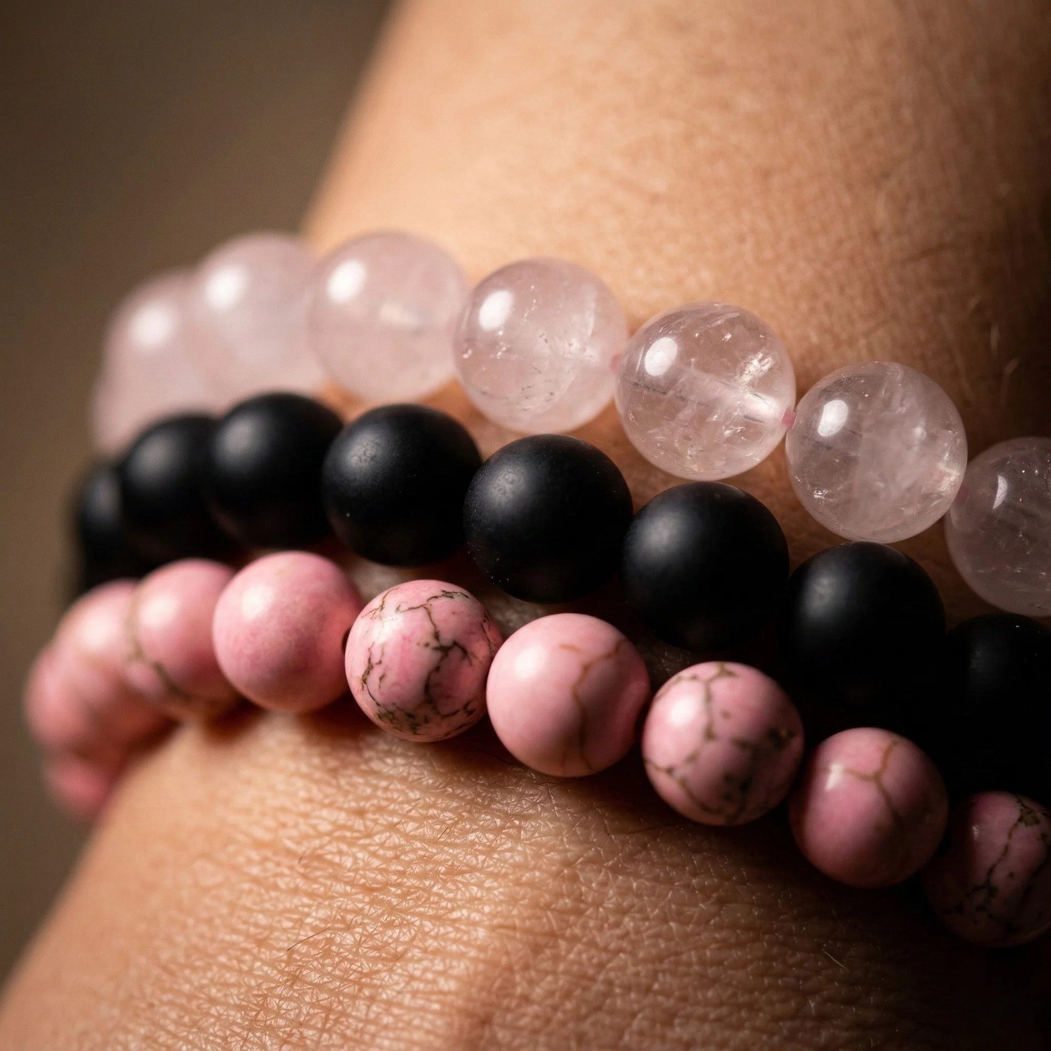 Close-up of a wrist wearing three beaded bracelets with pink, black, and rose quartz beads.