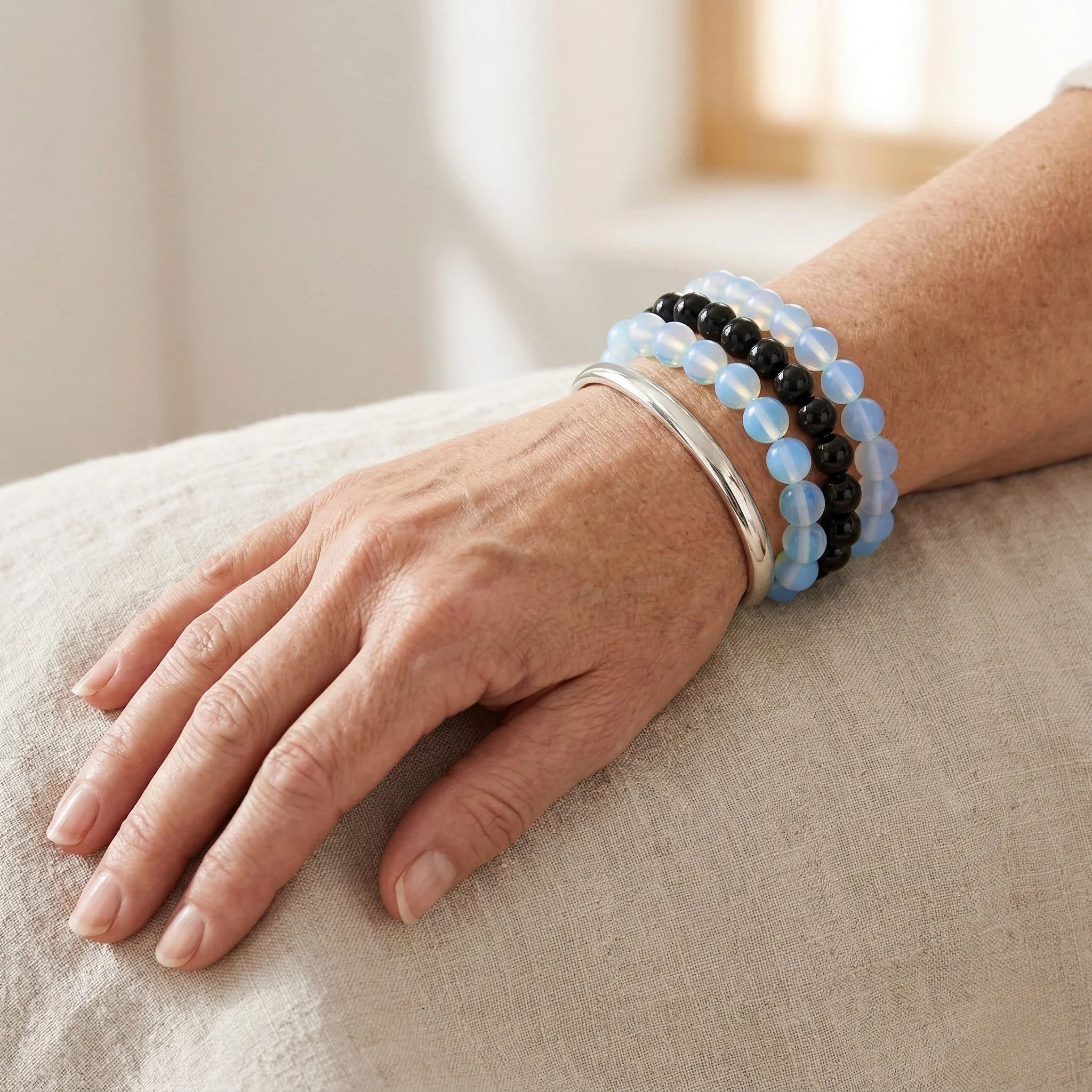 Hand wearing multiple bracelets on a neutral background