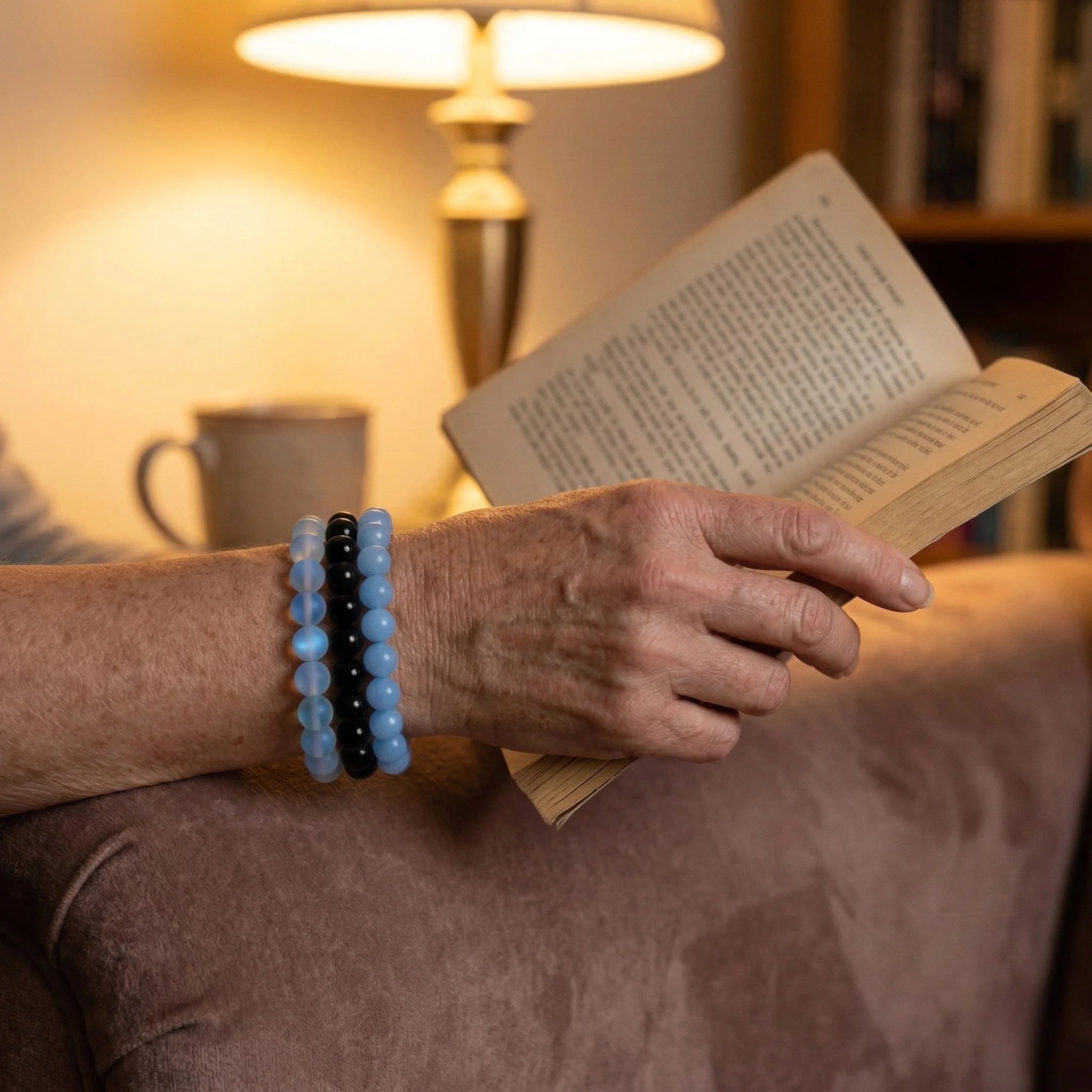 Person reading a book with a bracelet on wrist in a cozy indoor setting