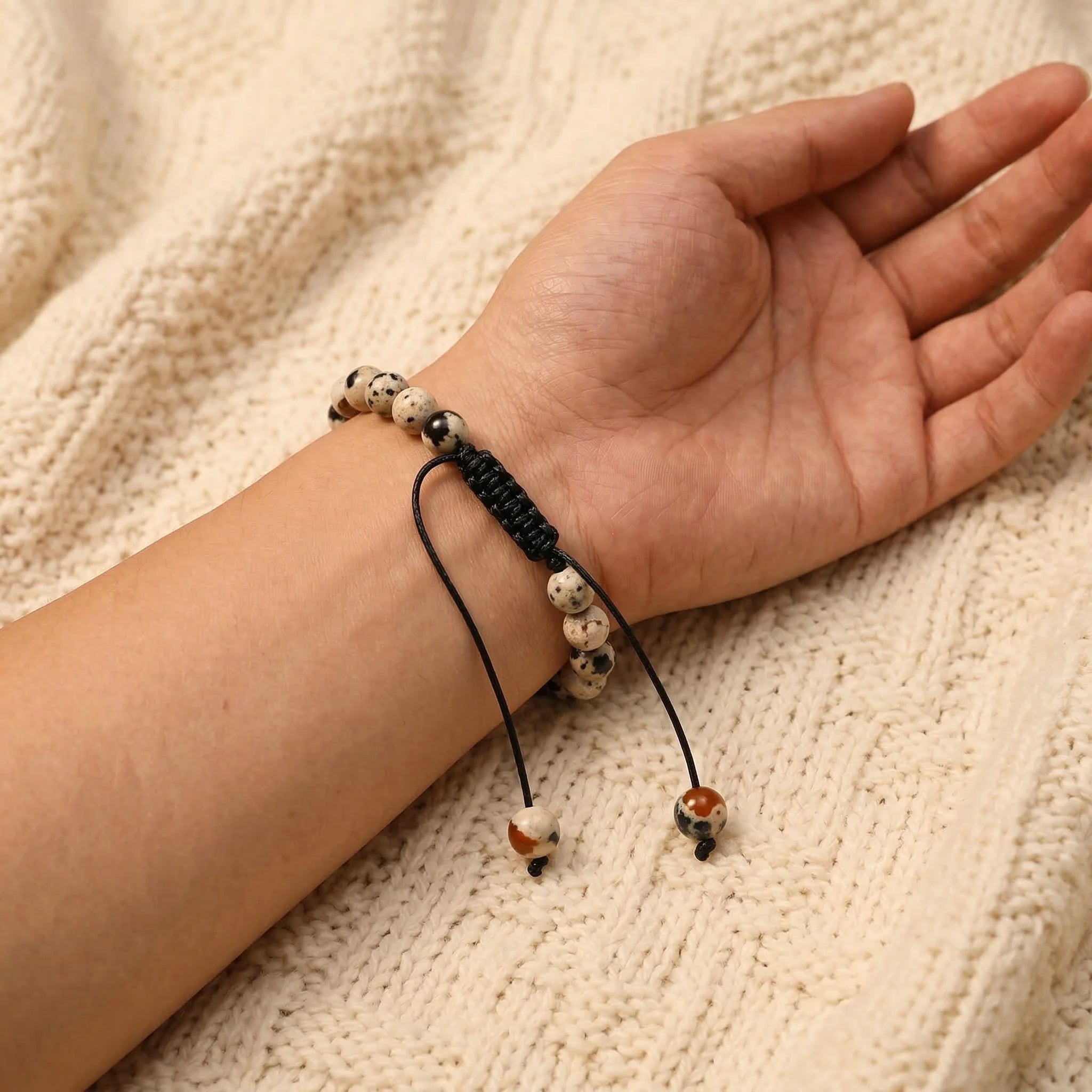 Hand wearing a bracelet with beads on a textured beige background