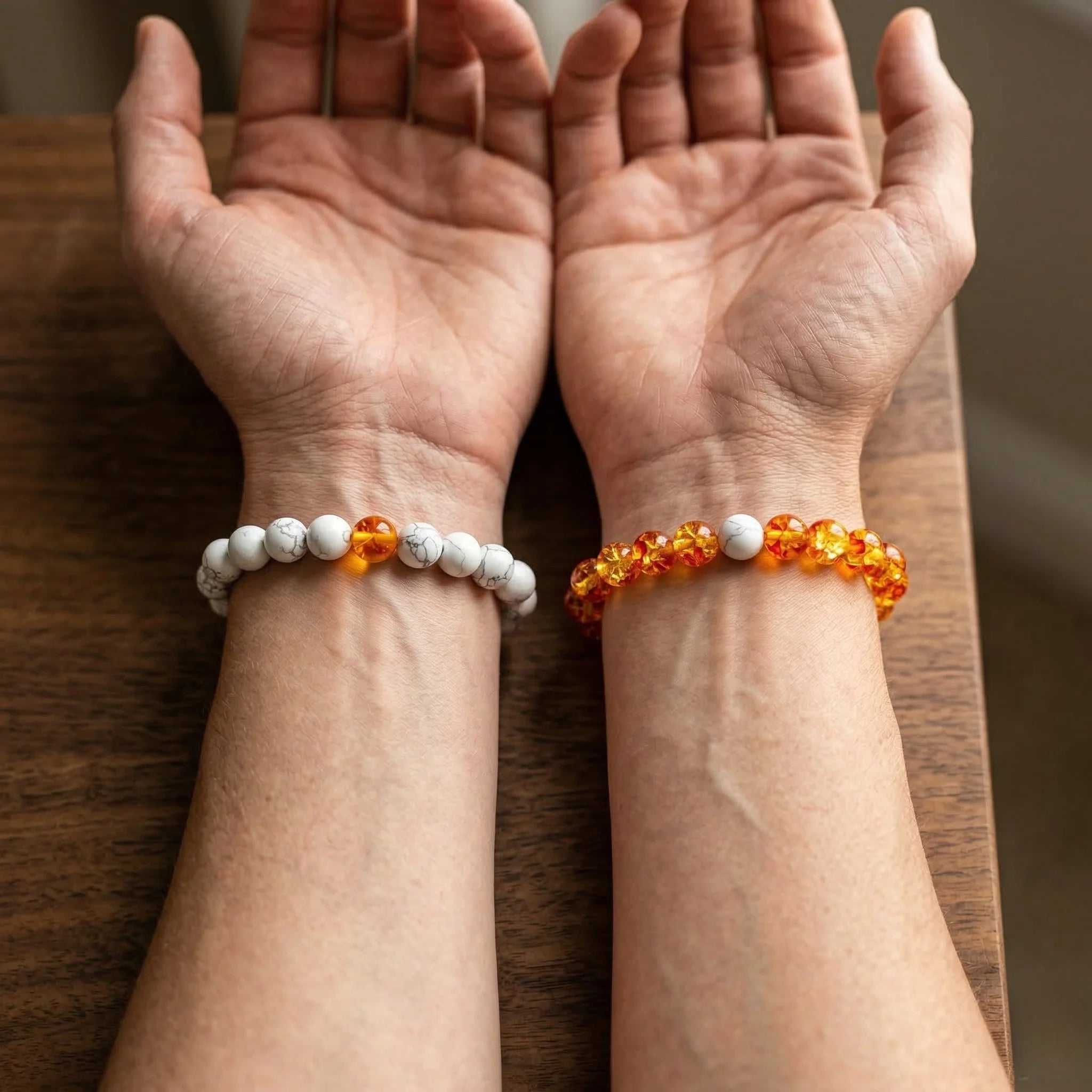 Two hands wearing beaded bracelets on a wooden surface
