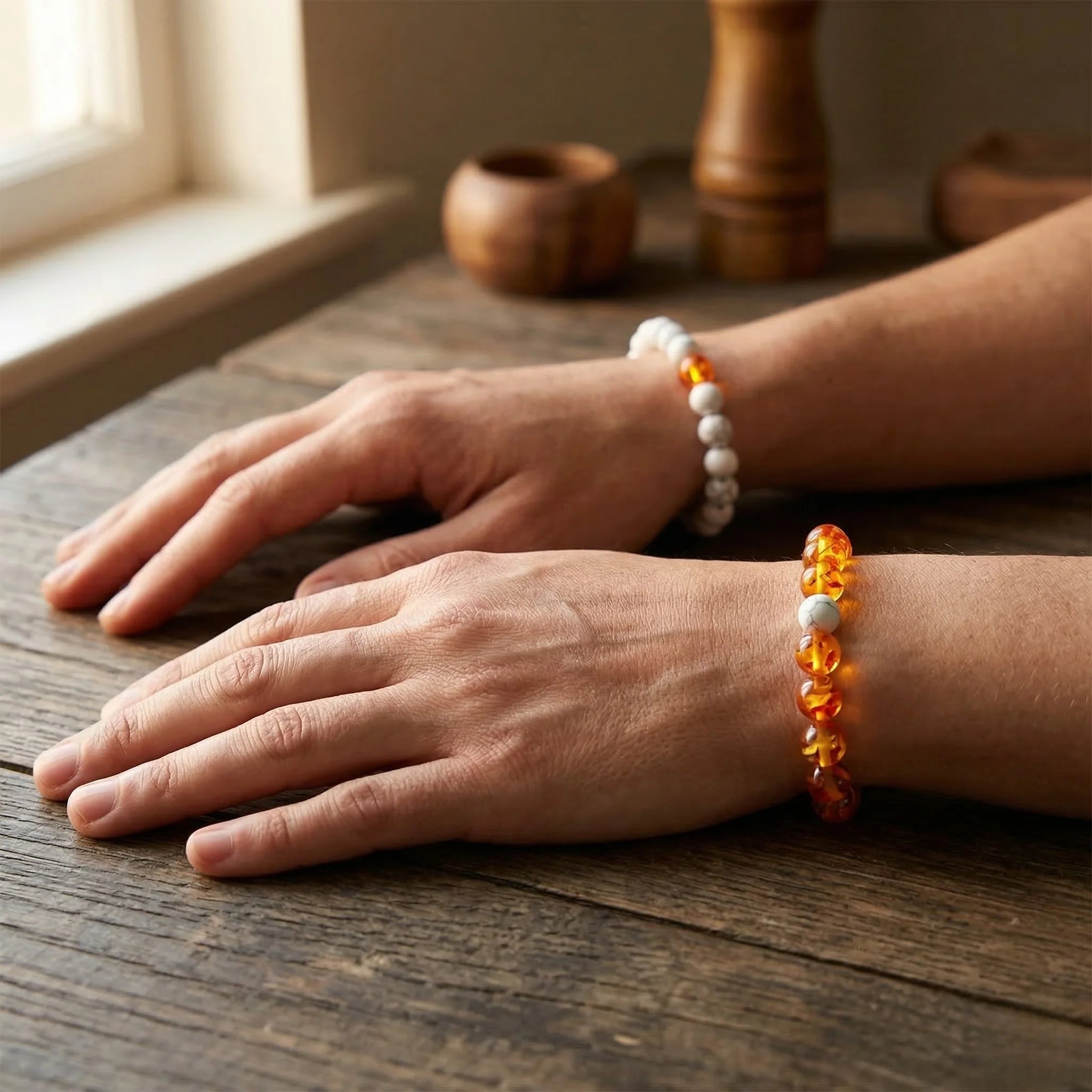 Two hands wearing beaded bracelets on a wooden surface with a warm, natural light setting.