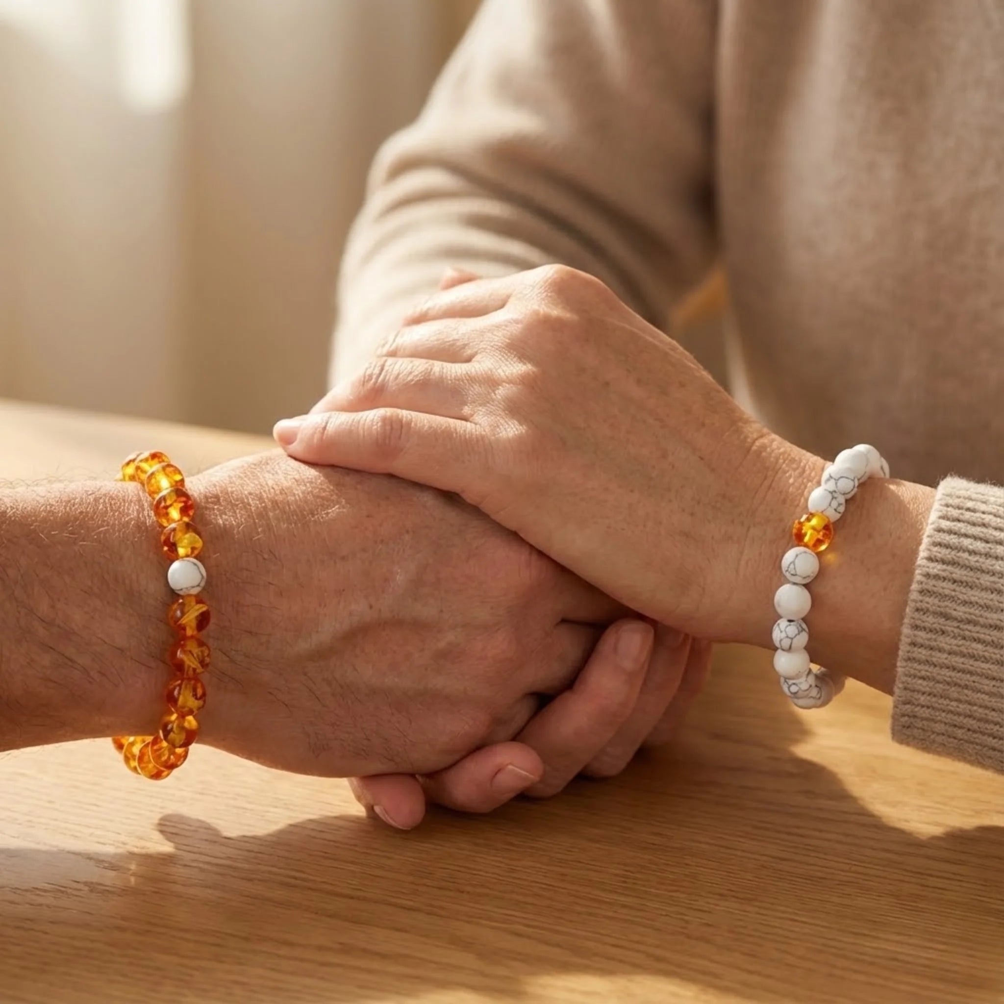 Two hands holding each other, wearing beaded bracelets on a wooden surface.