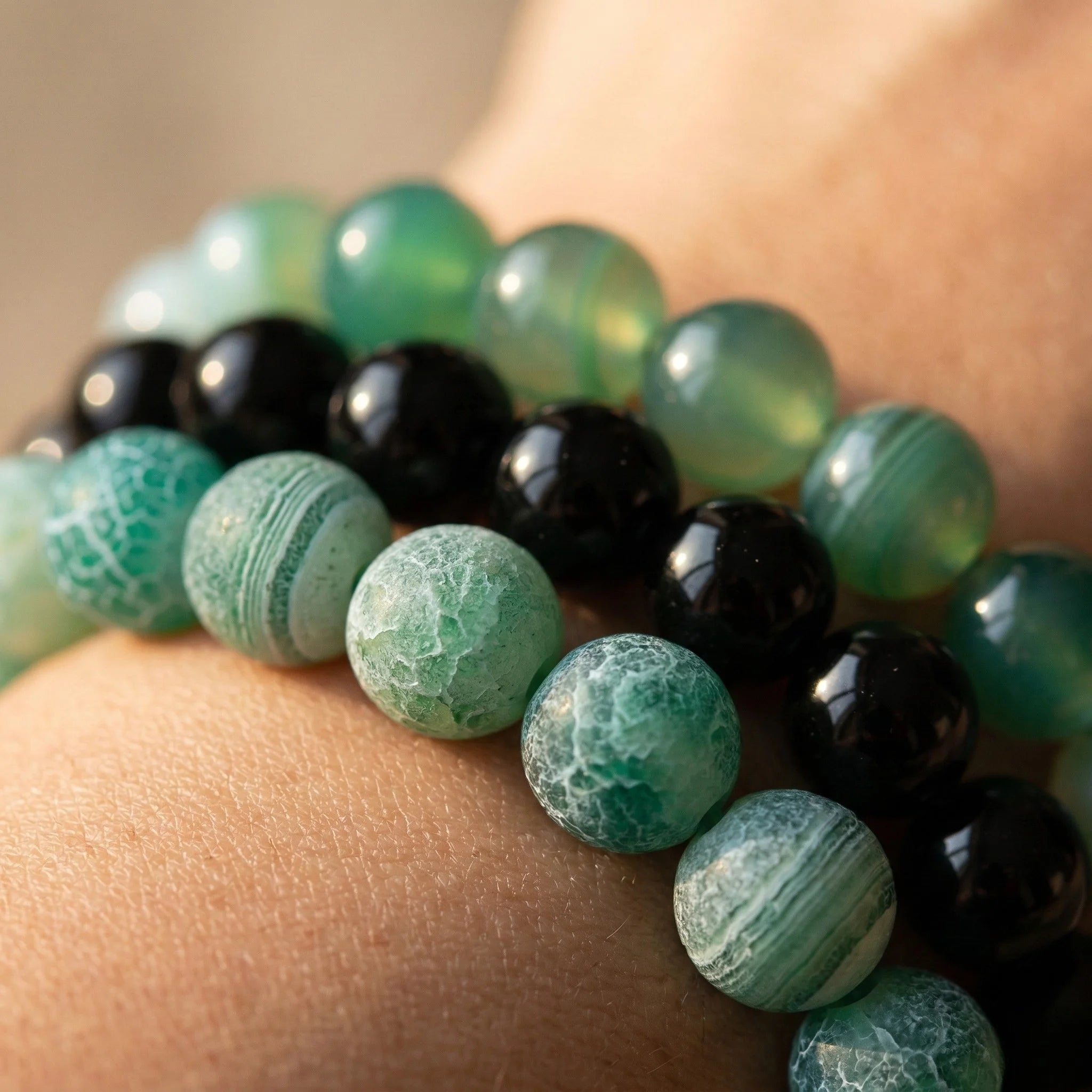 Close-up of a bracelet with green and black beads on a wrist.