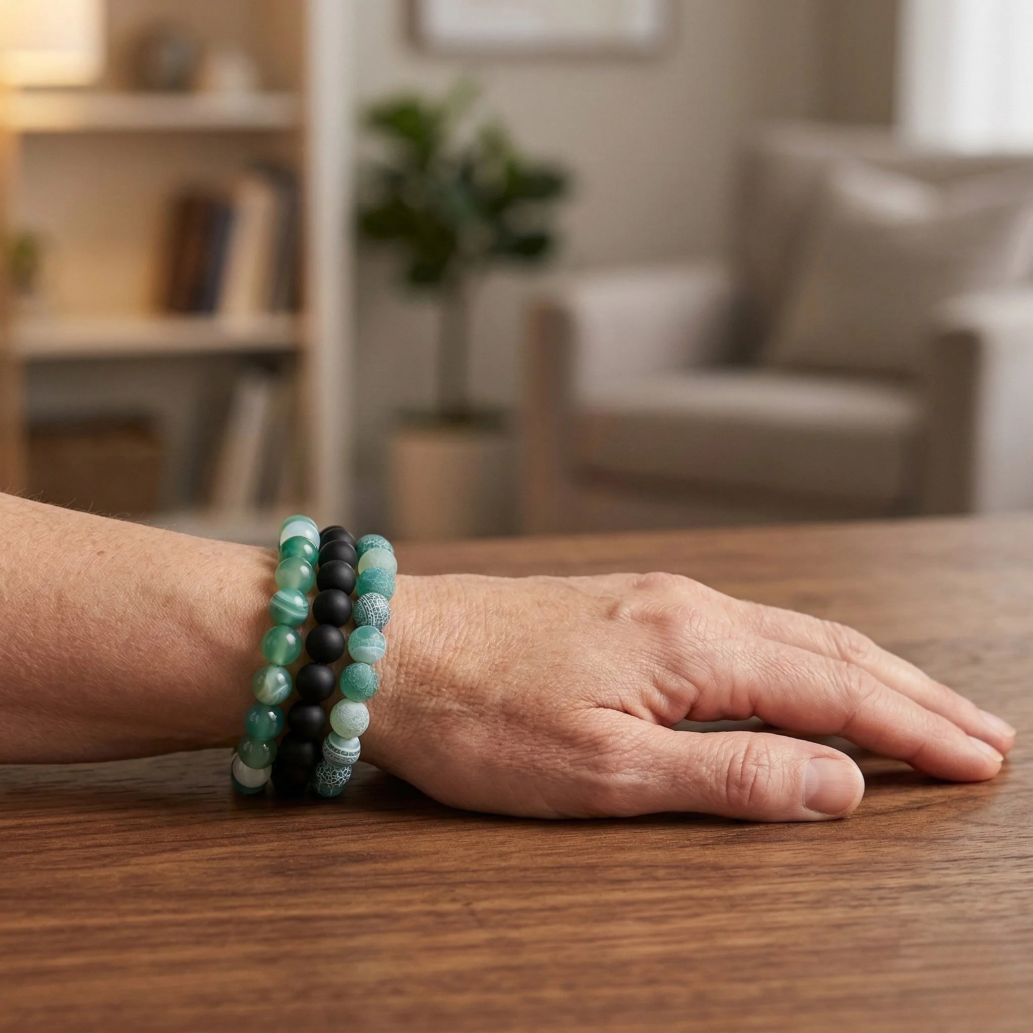Person wearing two bracelets on a wooden table with a blurred indoor background