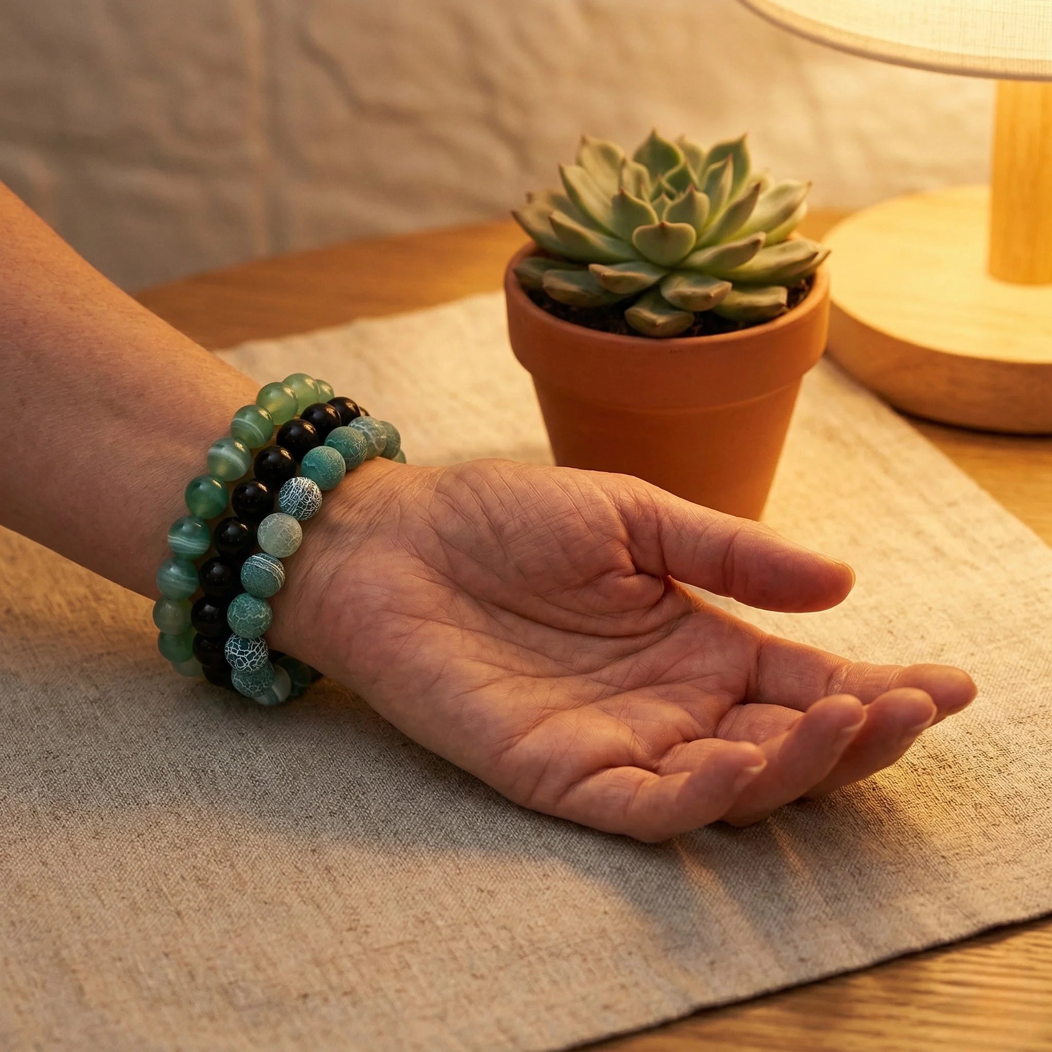 Hand wearing a green beaded bracelet with a potted succulent in the background