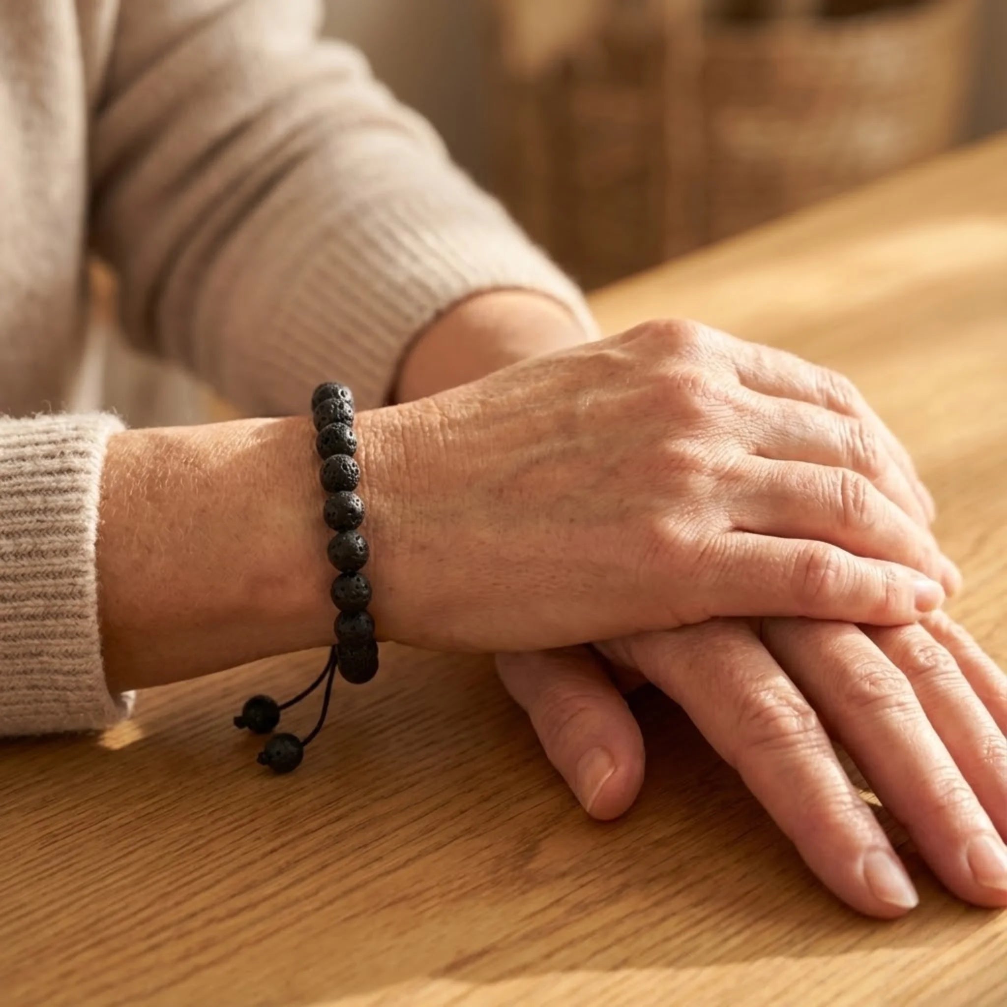 Close-up of a person's hands with a black beaded Adjustable balance bracelet made with black lava stone beads on a braided cord for a minimalist, grounded style bracelet on a wooden surface