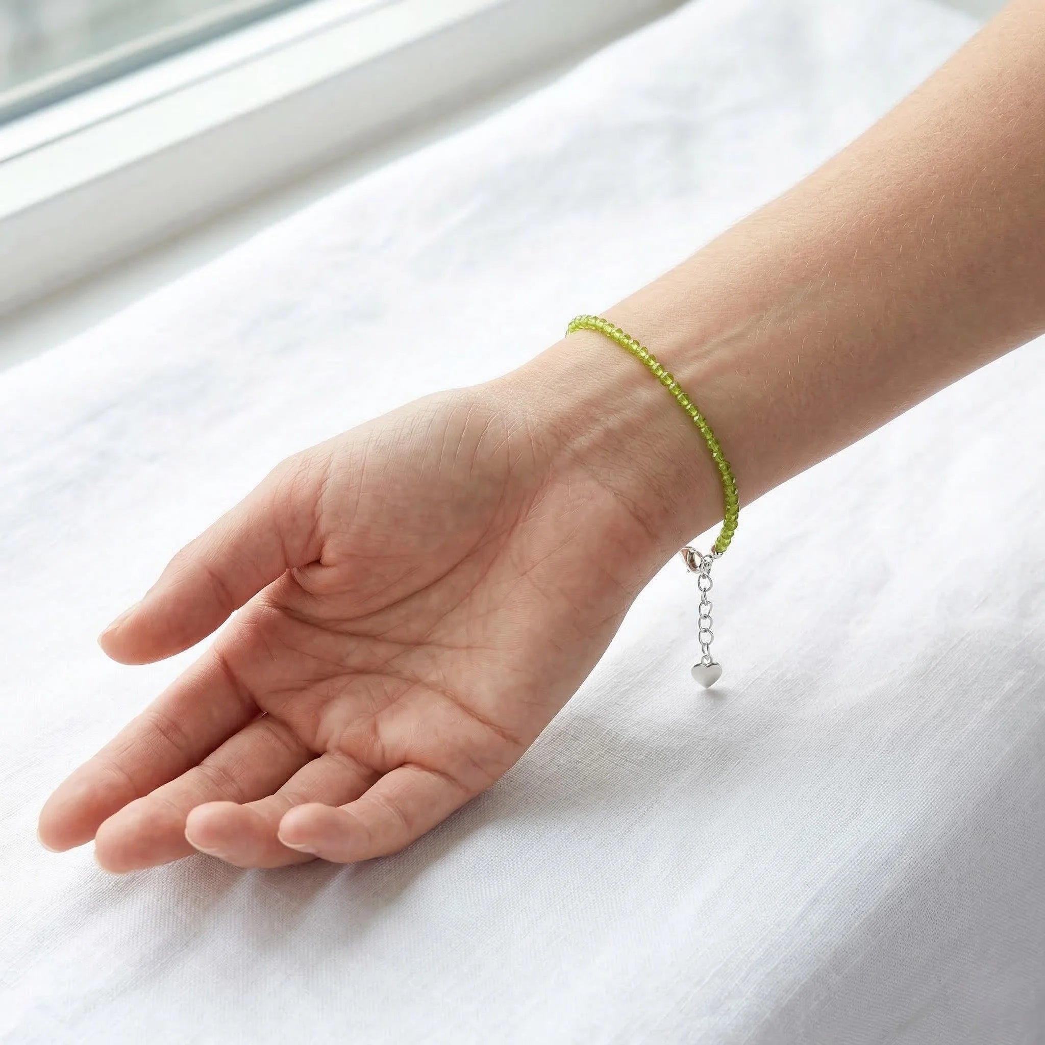 Hand wearing a green beaded bracelet on a white surface