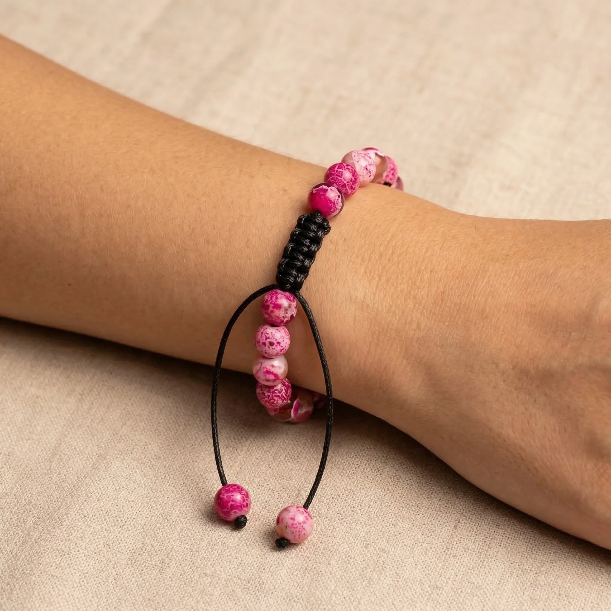Pink beaded bracelet on a wrist against a beige background