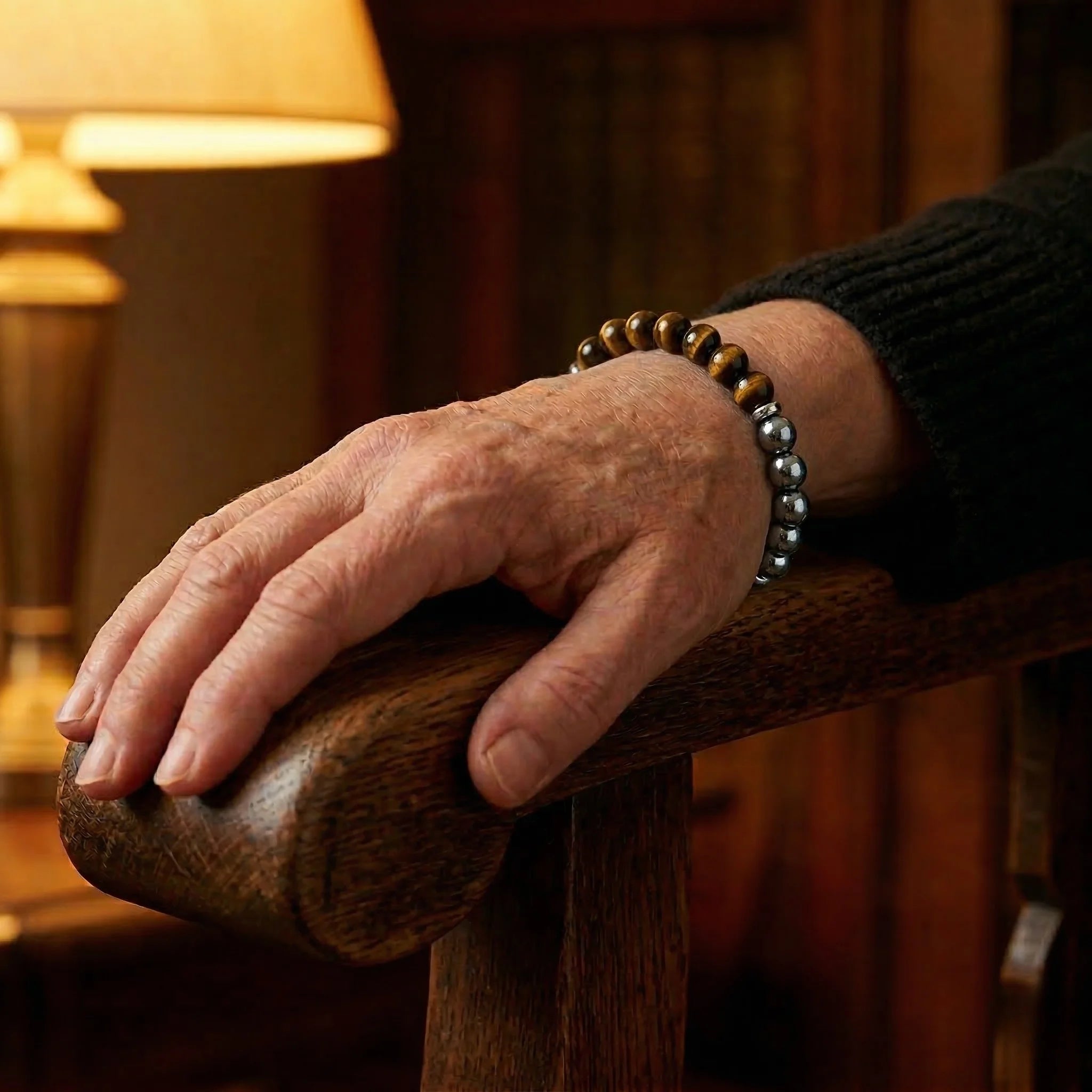 Hand with a bracelet on a wooden armrest in a warm, indoor setting