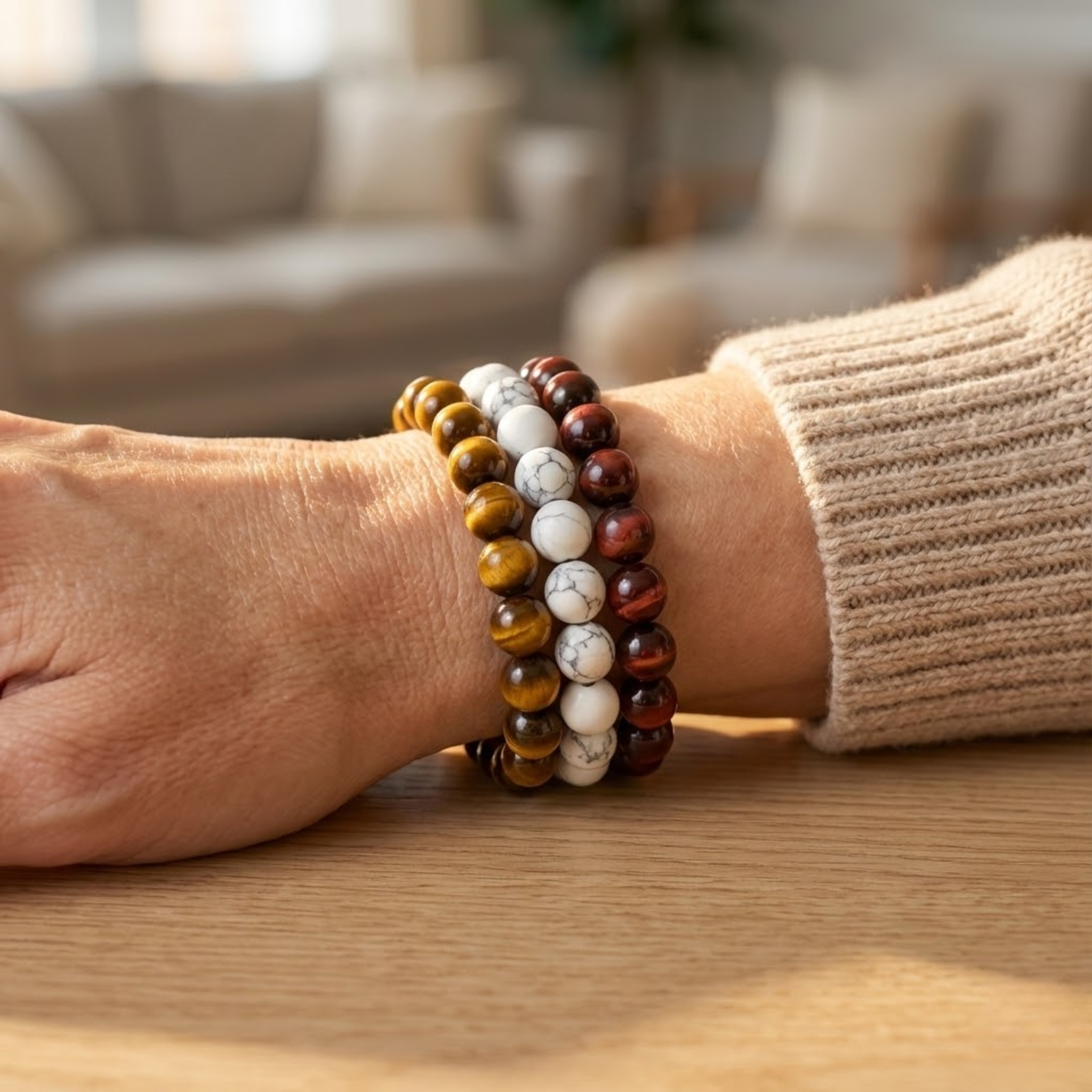 Person wearing a stack of beaded Resilience intention bracelet stack featuring tiger eye and imitation howlite beads symbolizing bravery and emotional resilience bracelets on a wooden surface with a blurred indoor background