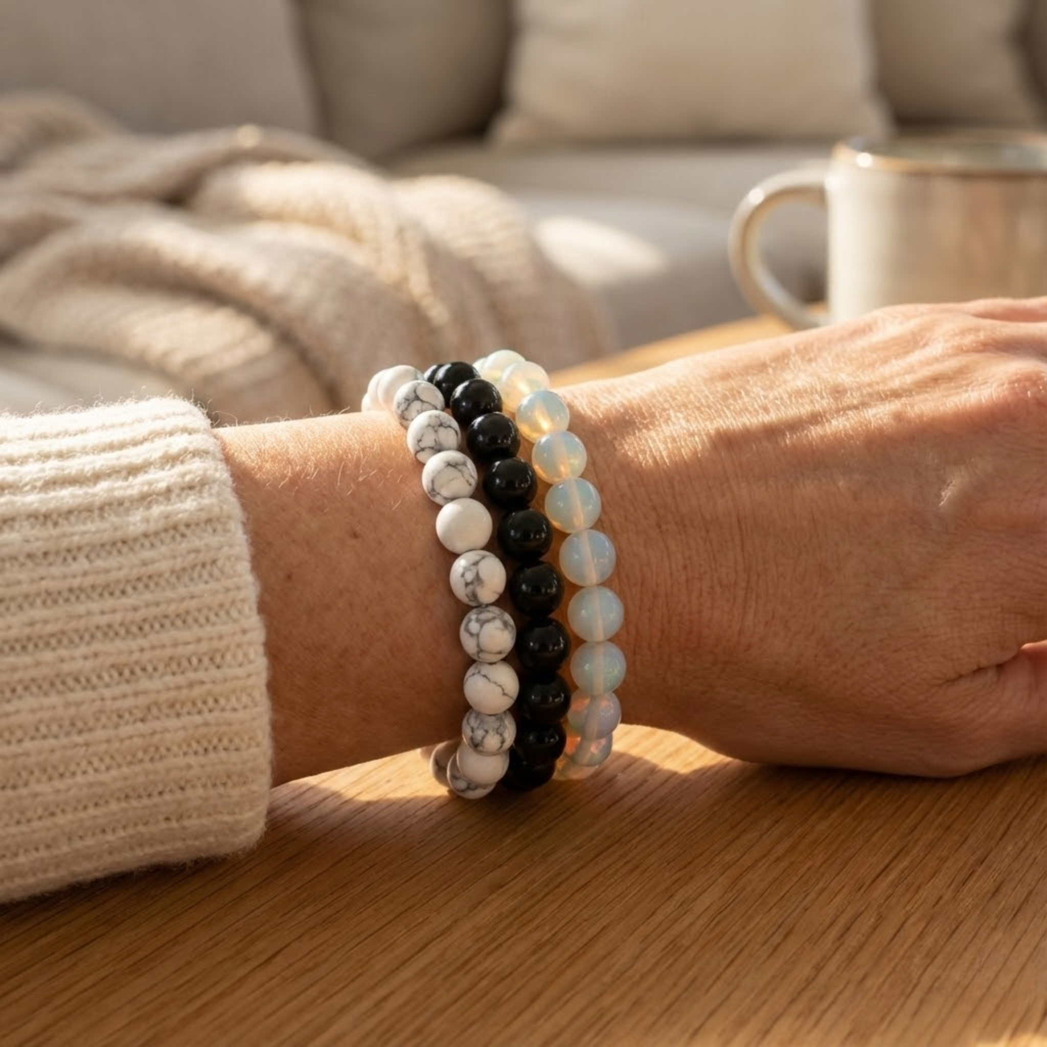 Person wearing three beaded Serenity intention bracelet stack with white howlite, black onyx, and opal beads for calm energy and clarity bracelets on a wooden surface with a blurred background