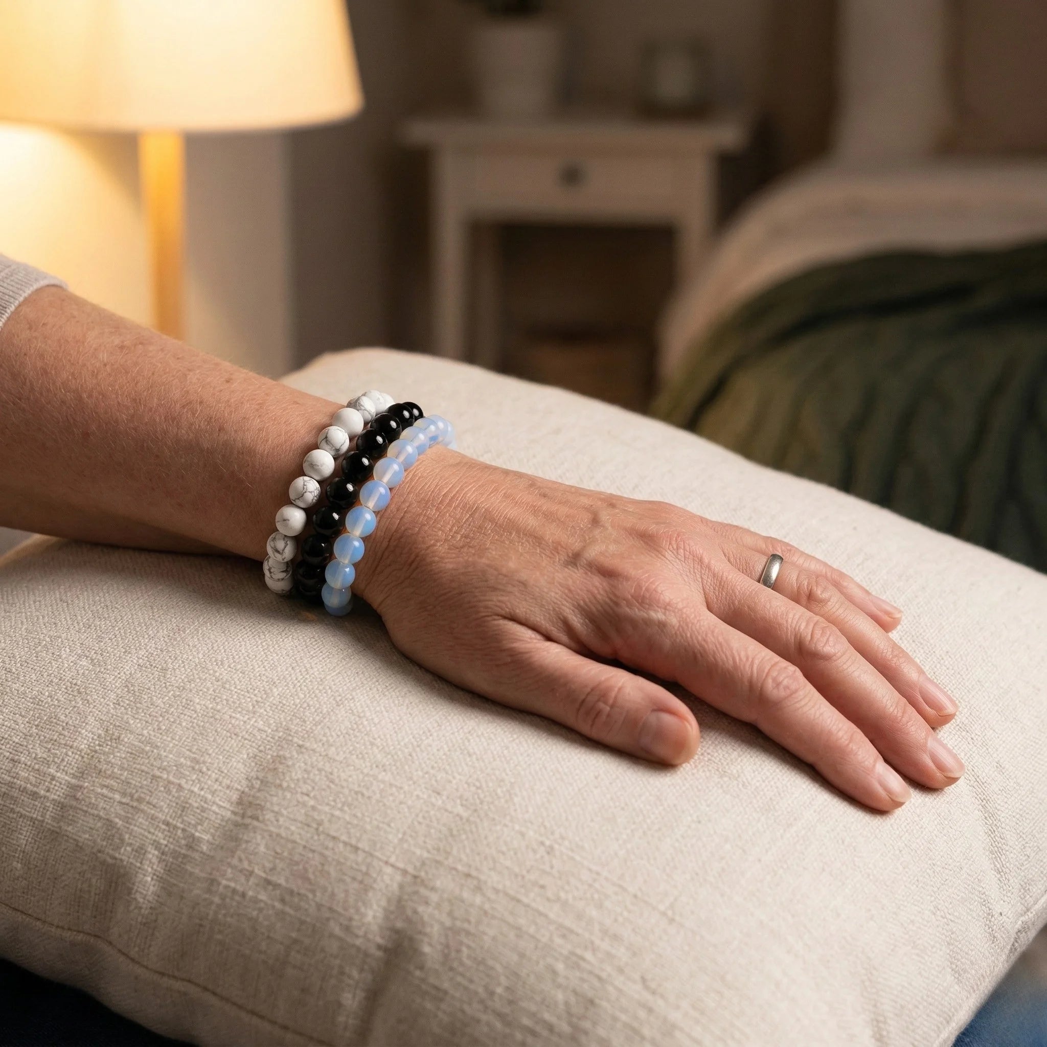 Hand wearing a bracelet on a pillow with a blurred bedroom background