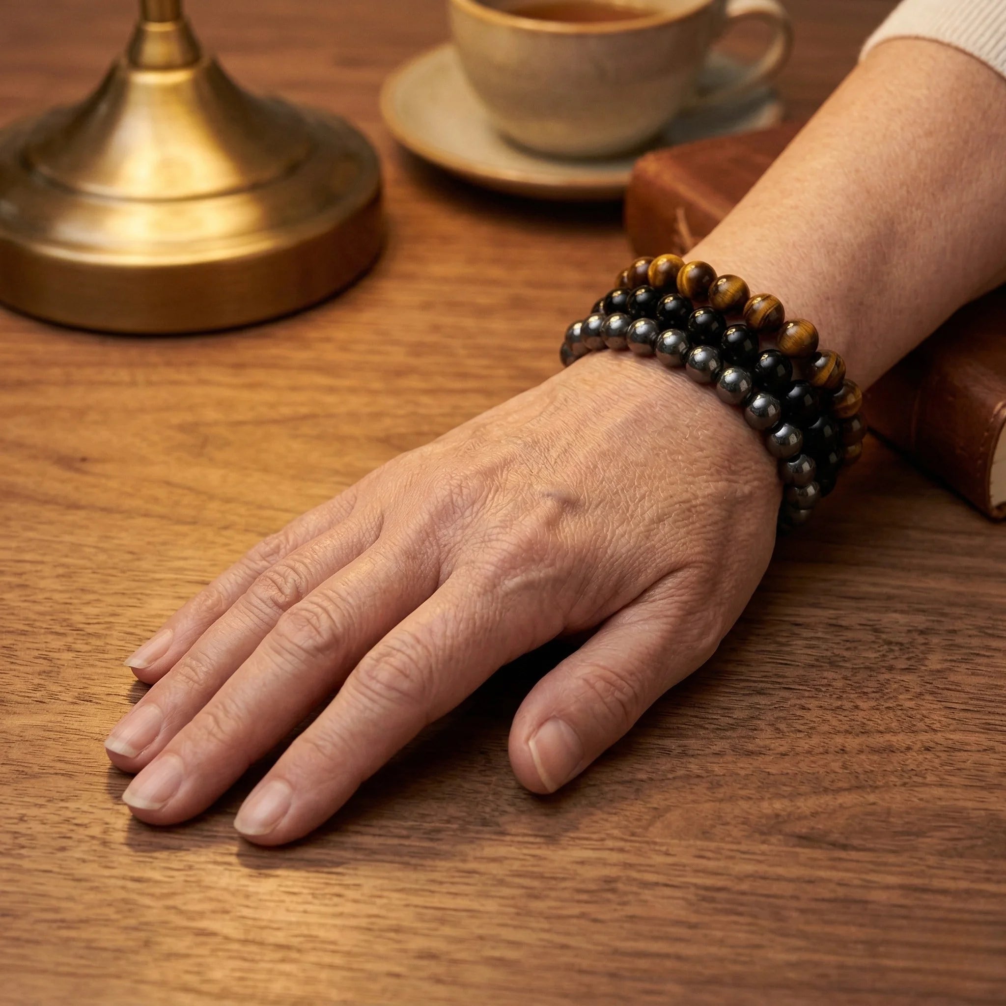 Hand wearing a beaded bracelet on a wooden table with a cup and saucer in the background