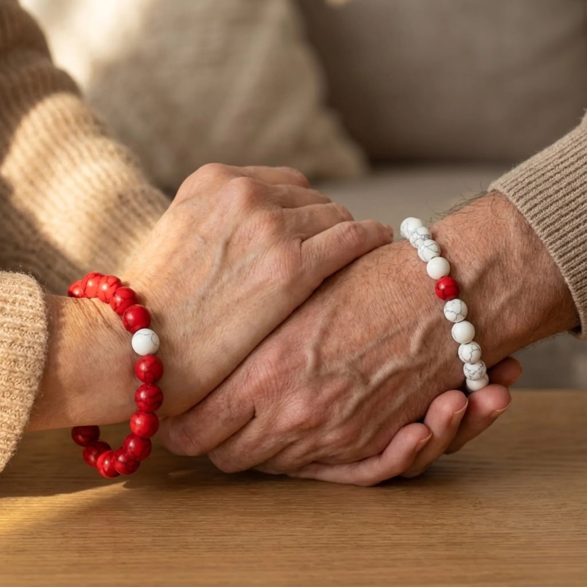 Two pairs of hands holding each other, wearing red and white beaded bracelets.
