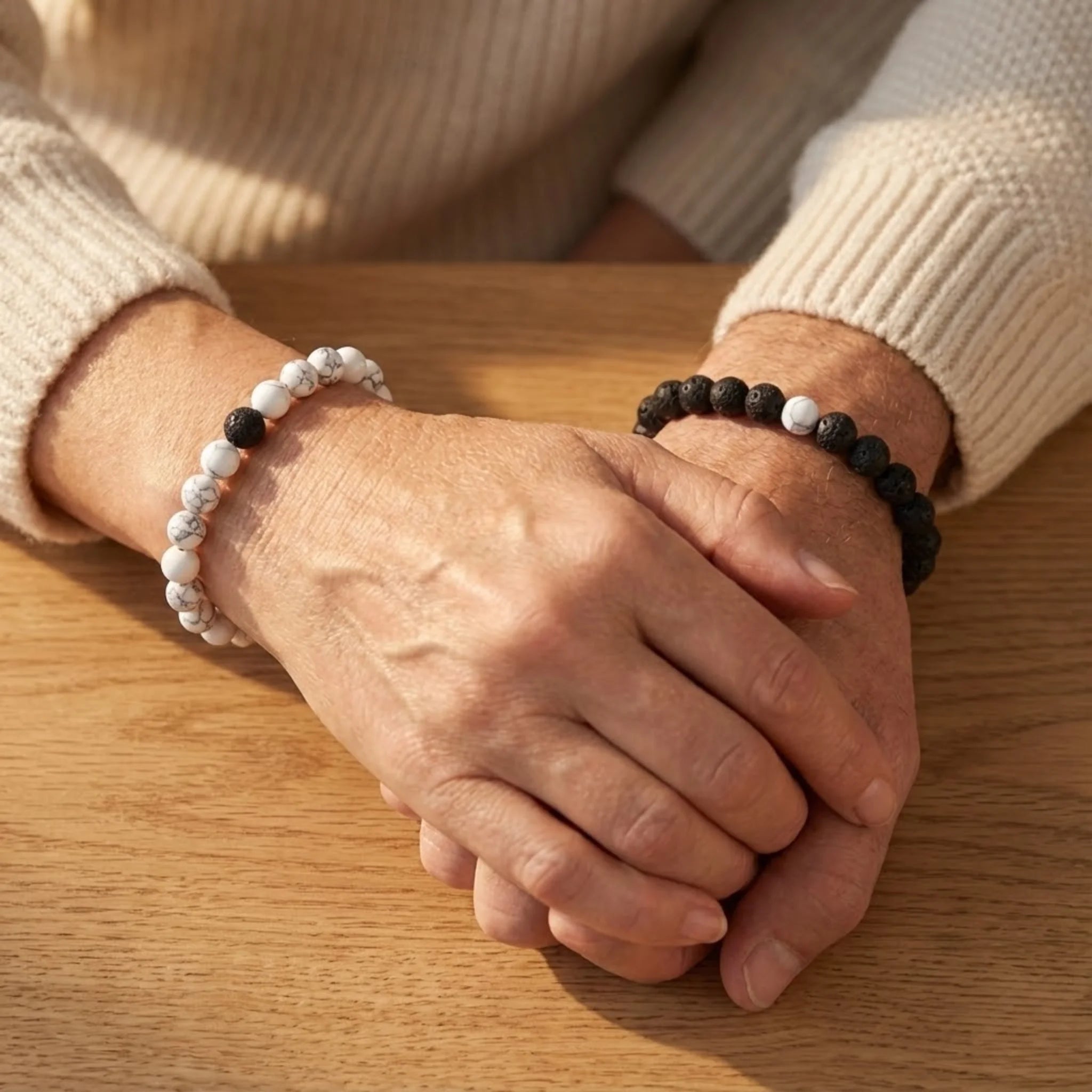 Close-up of hands wearing black and white beaded bracelets on a wooden surface.