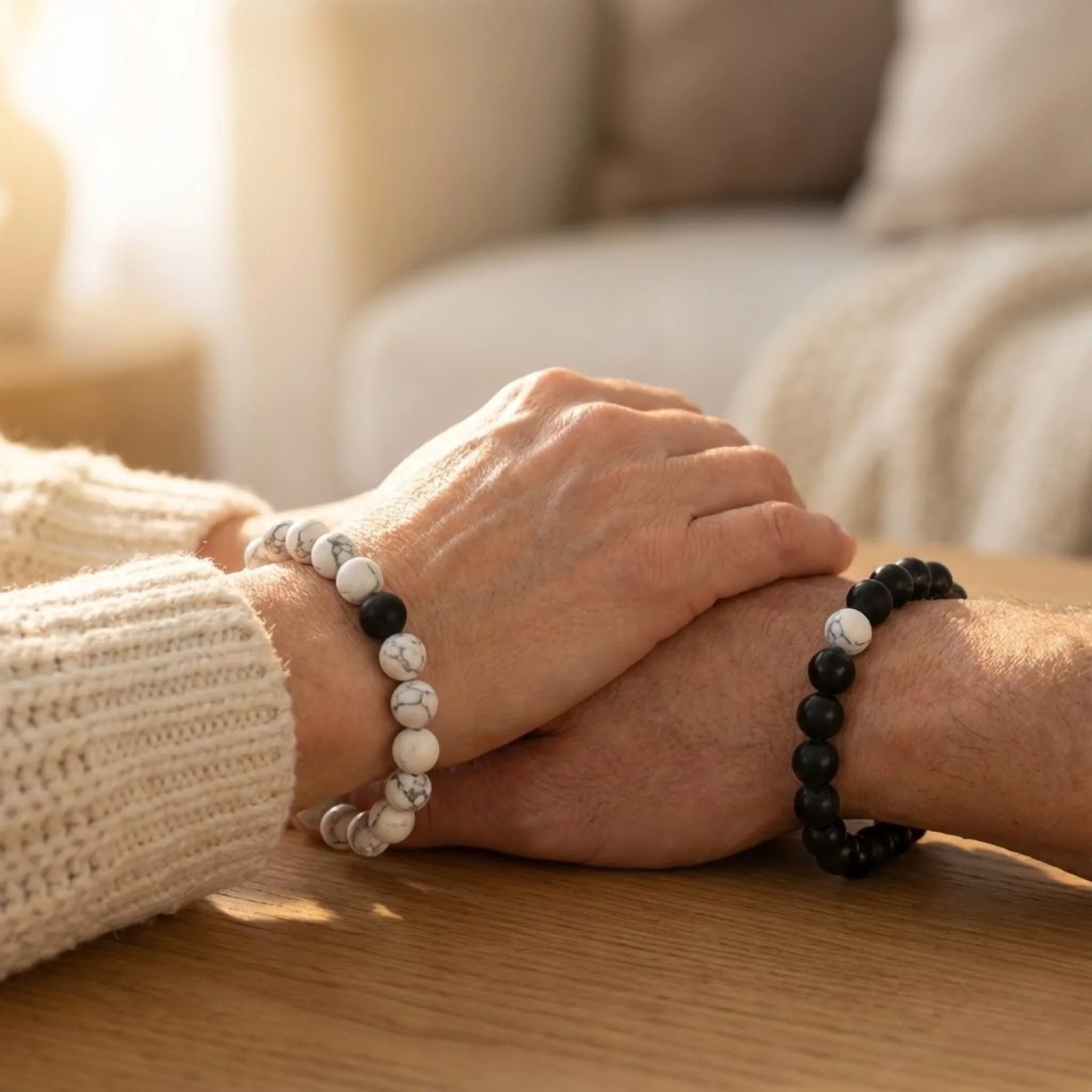 Two hands wearing beaded bracelets on a wooden surface with a blurred background