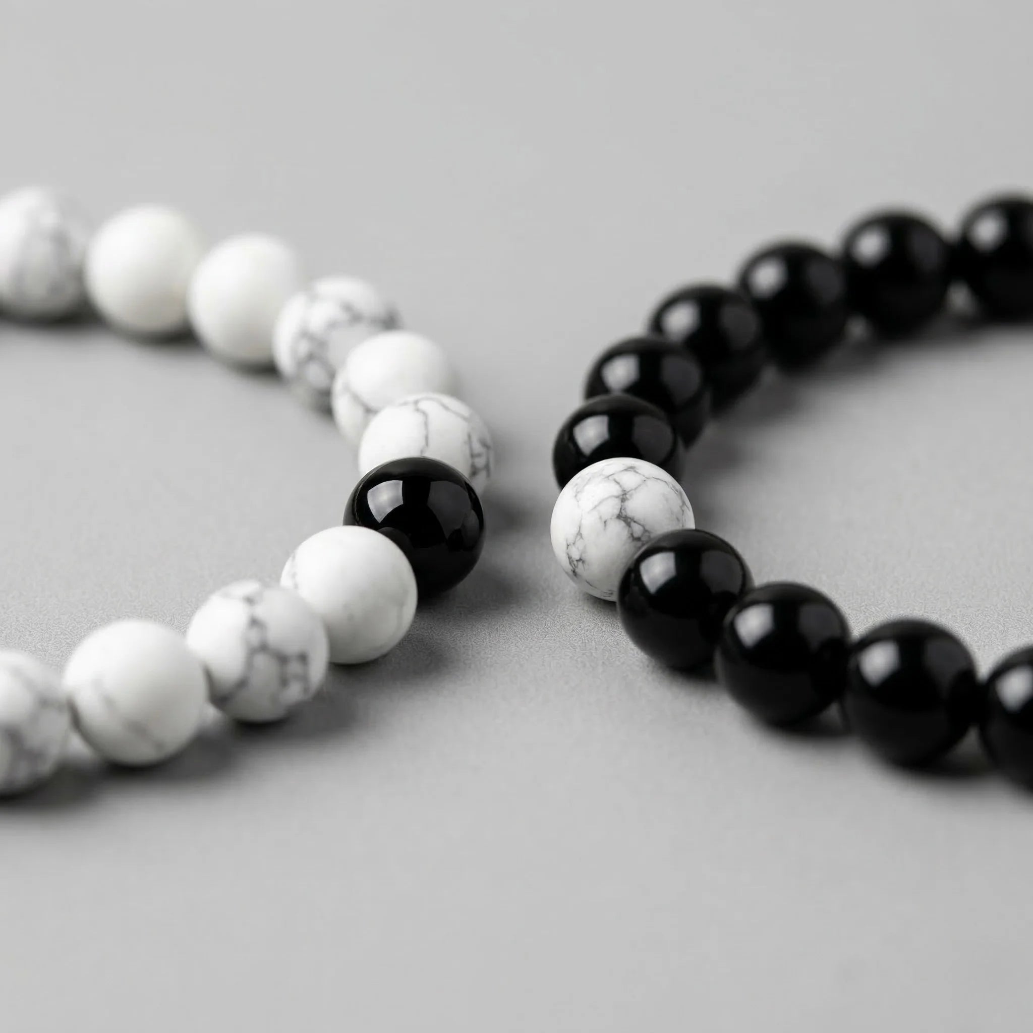 Two beaded bracelets, one with white and black beads and the other with black beads, on a light gray background.