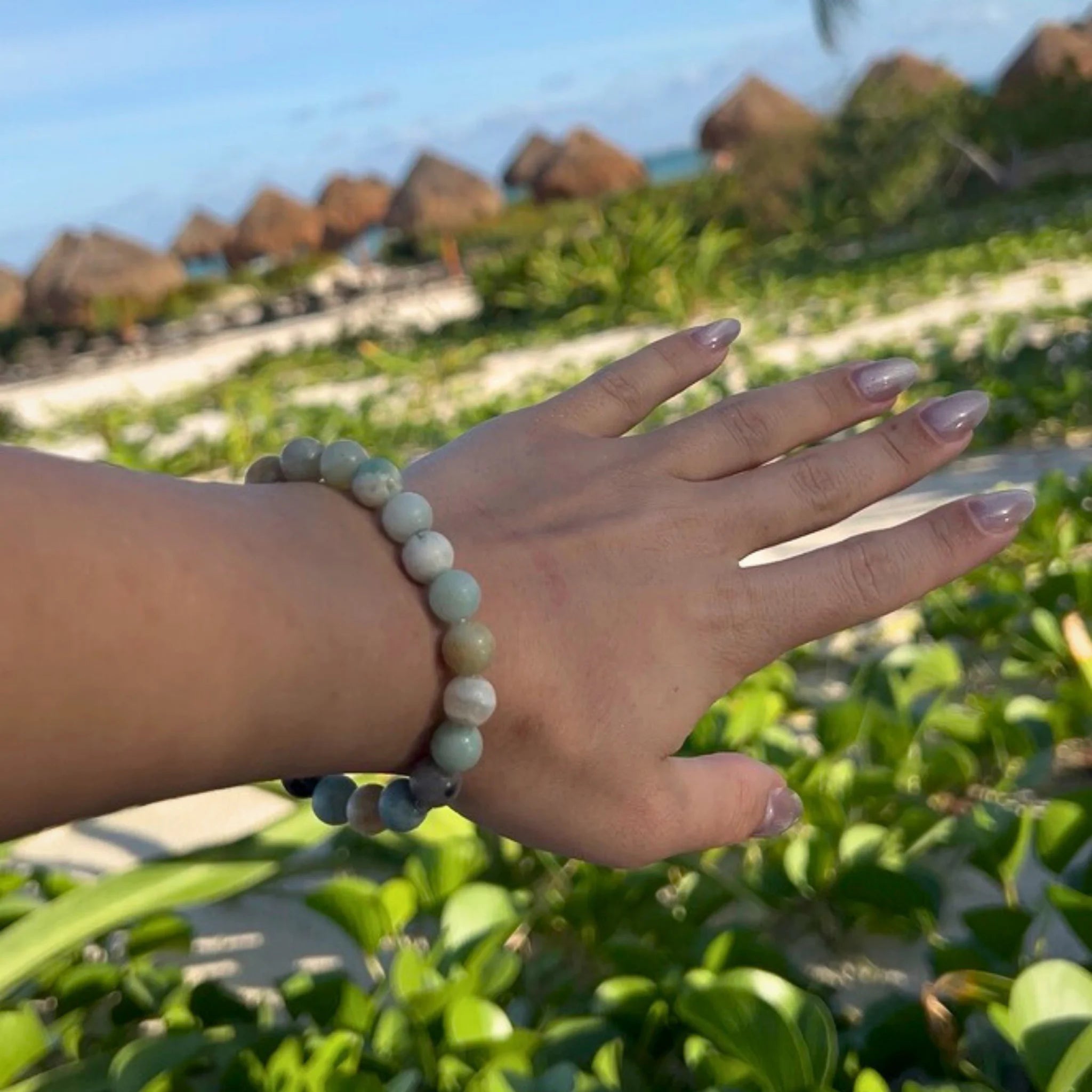 Gemstone4K amazon stone bracelet worn on wrist near beach or sunlight, showing aqua tones and reflective polish.