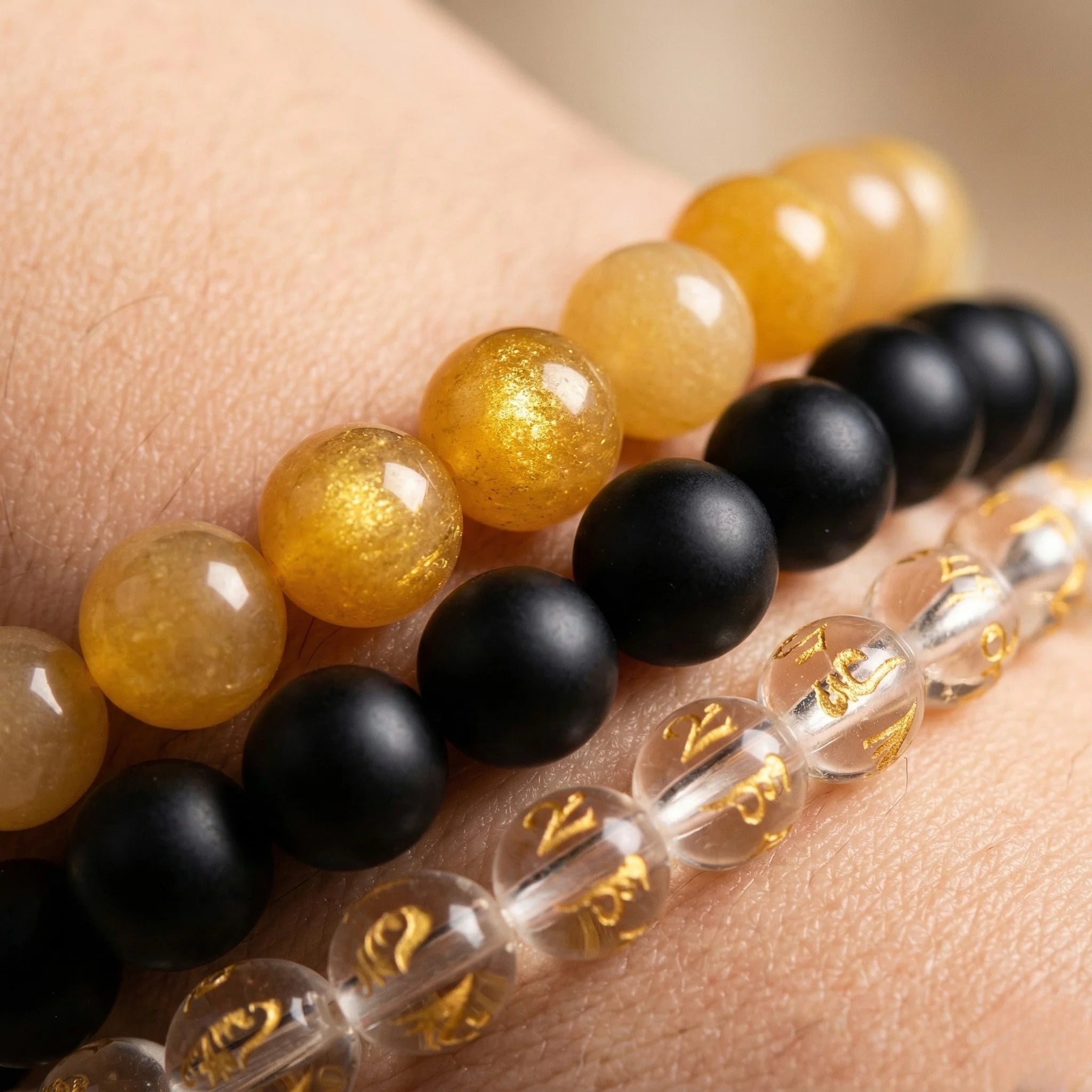Close-up of a person wearing three beaded bracelets with yellow, black, and clear beads.
