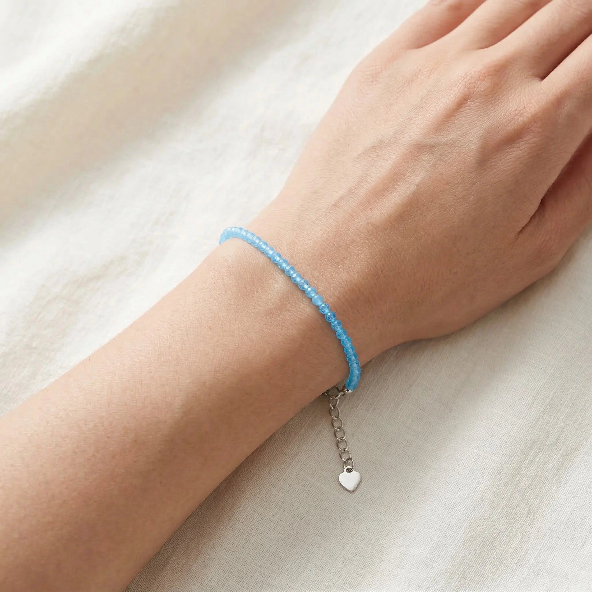 Hand wearing a blue bracelet with a heart charm on a light background