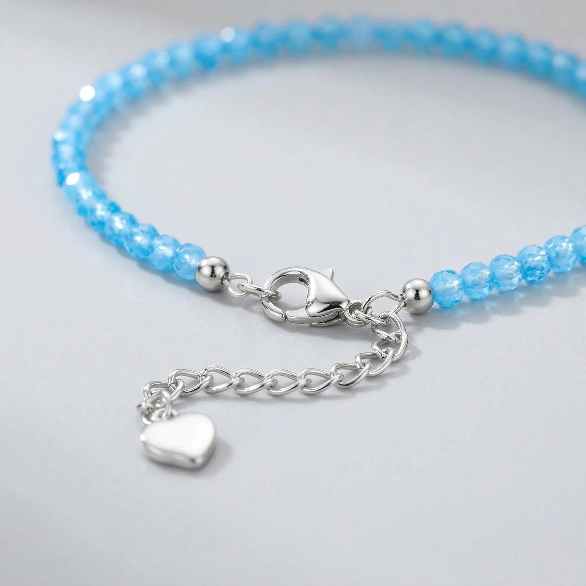 Blue beaded bracelet with a silver clasp and heart charm on a light gray background