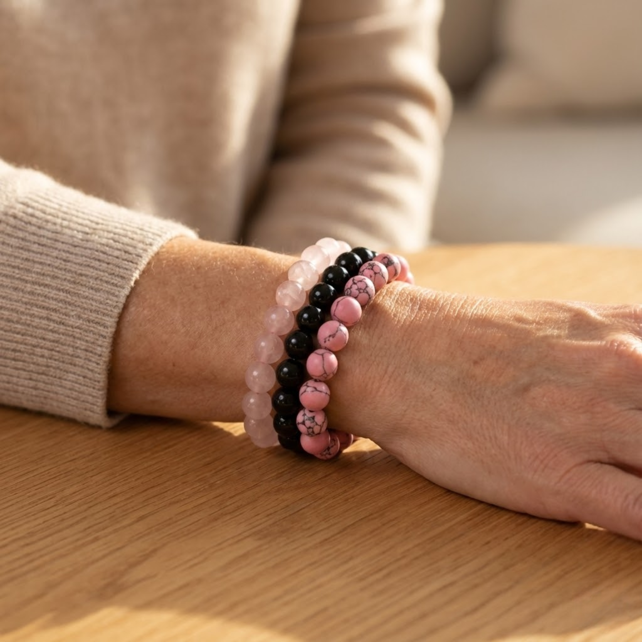 Person wearing a bracelet with pink and black Benevolence intention bracelet stack with rose pink quartz, black onyx, and pink imitation turquoise beads for love and kindness beads on a wooden surface