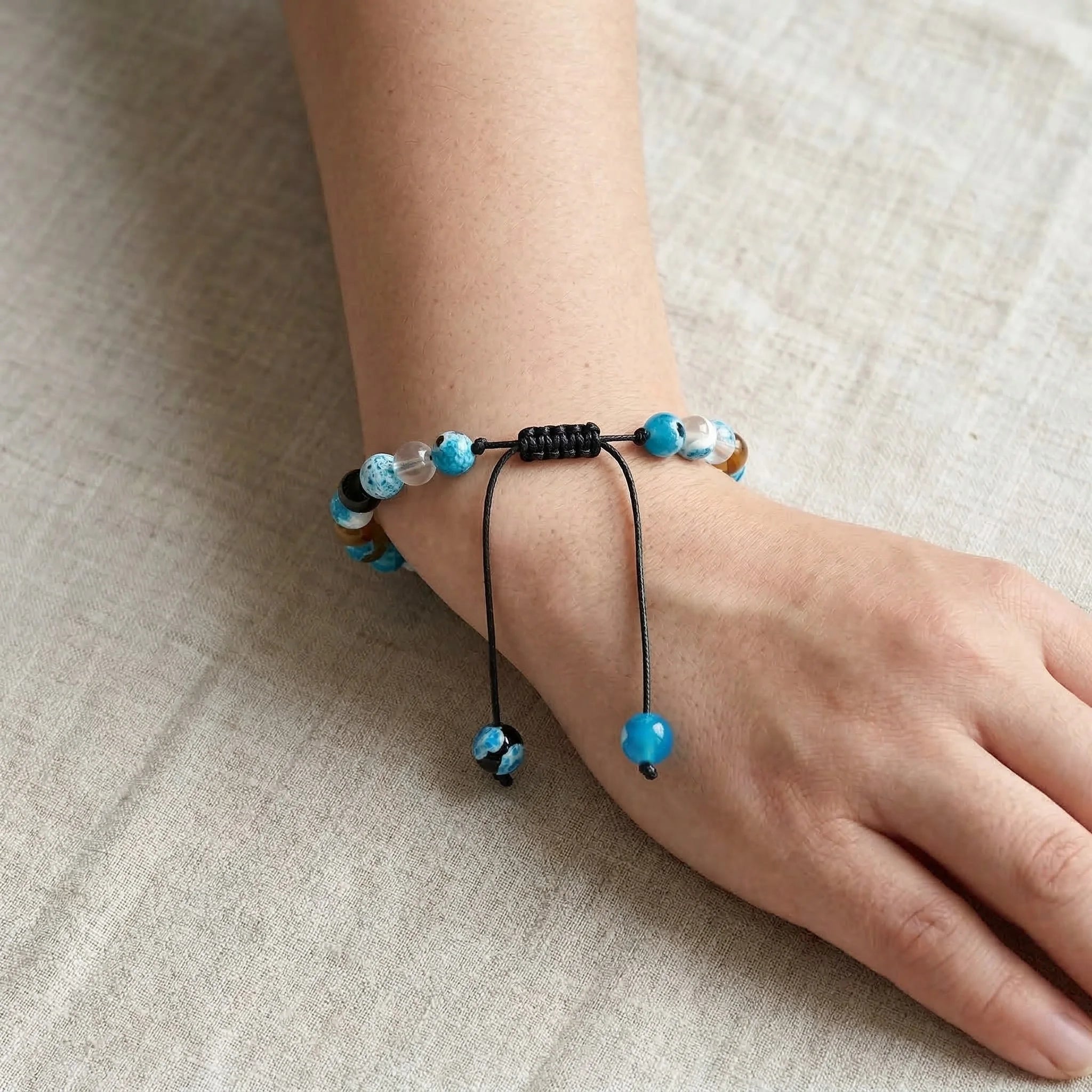 Hand wearing a bracelet with blue beads on a beige fabric background