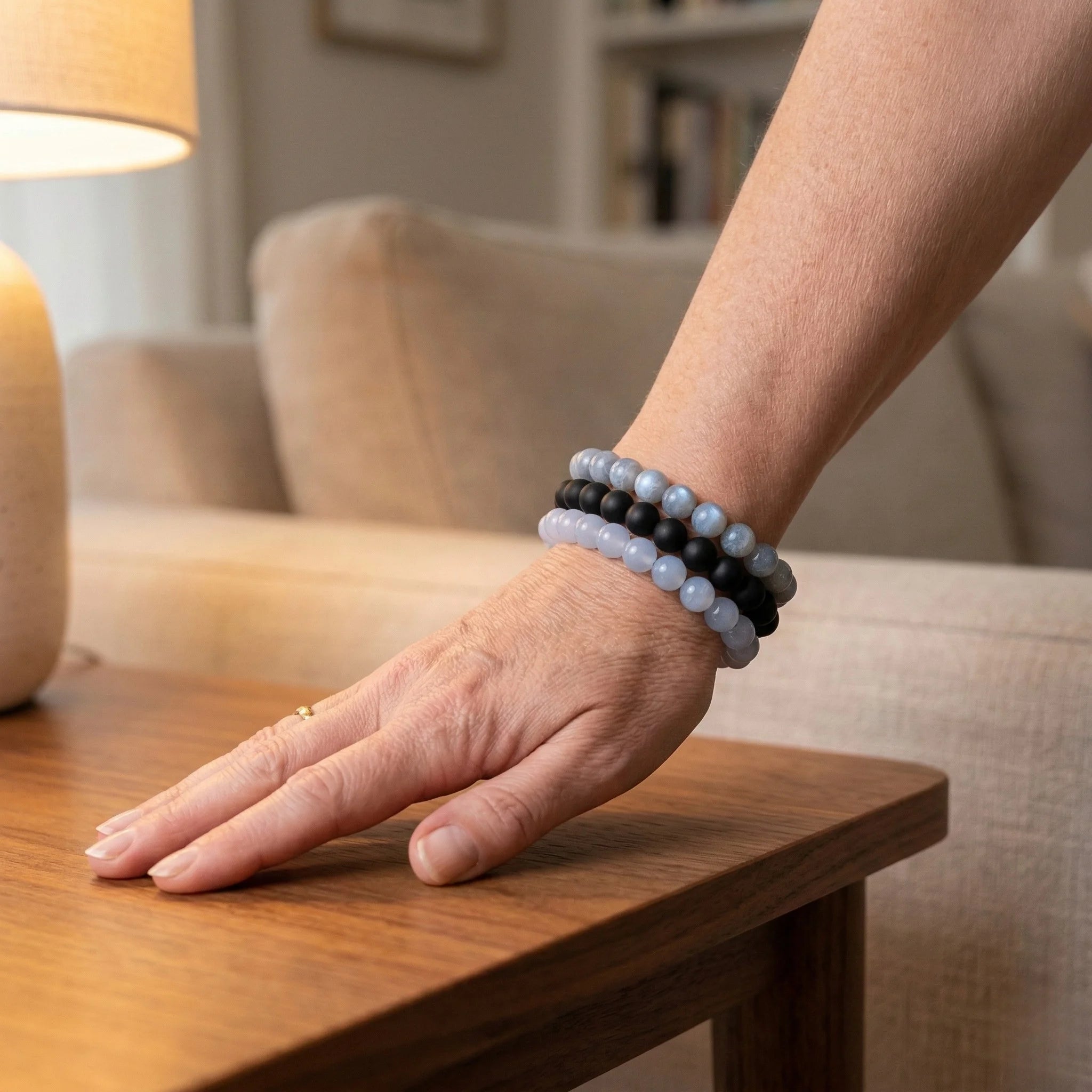 Person wearing multiple beaded bracelets on a hand resting on a wooden table with a blurred indoor background