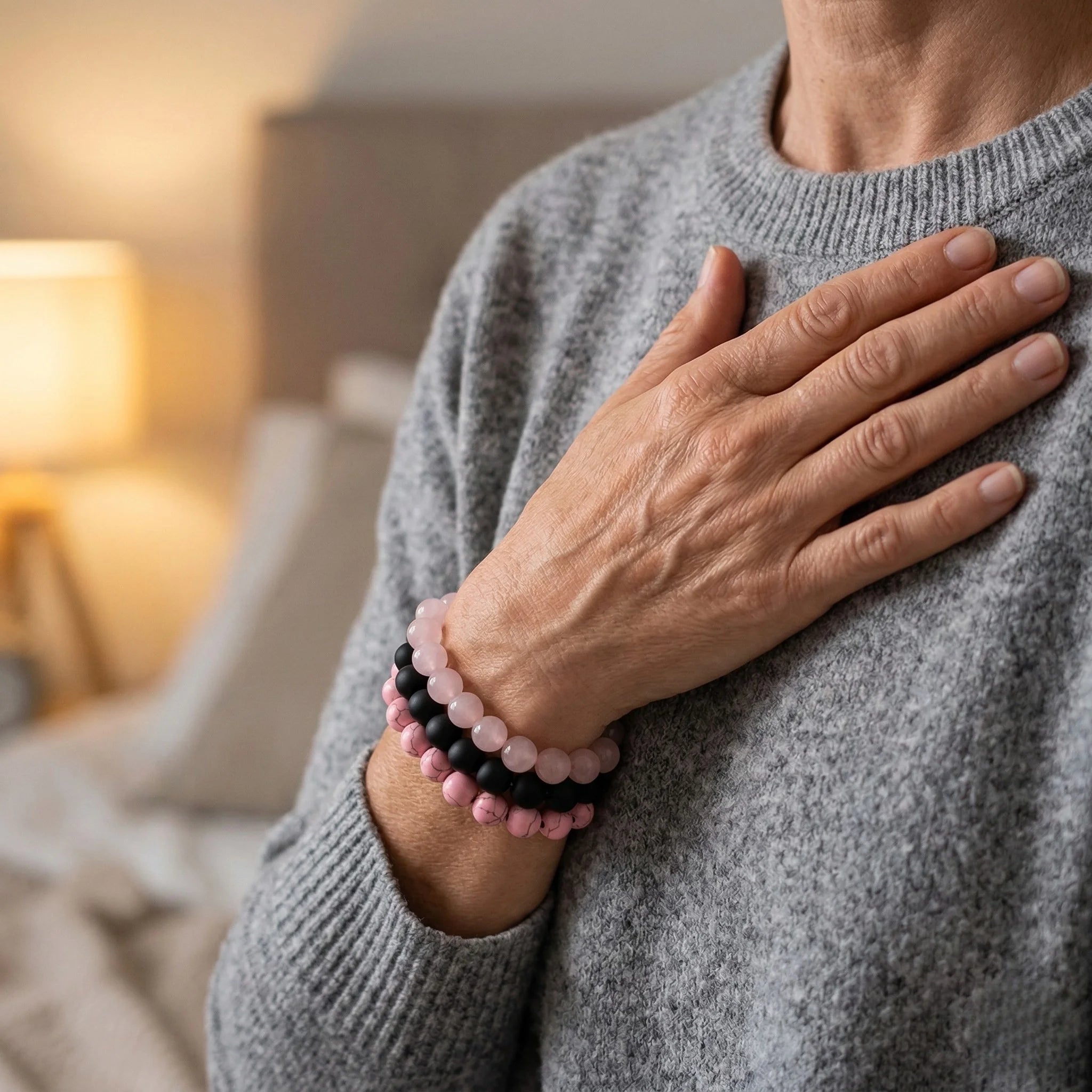 Person wearing a gray sweater with a pink and black beaded bracelet on a blurred indoor background