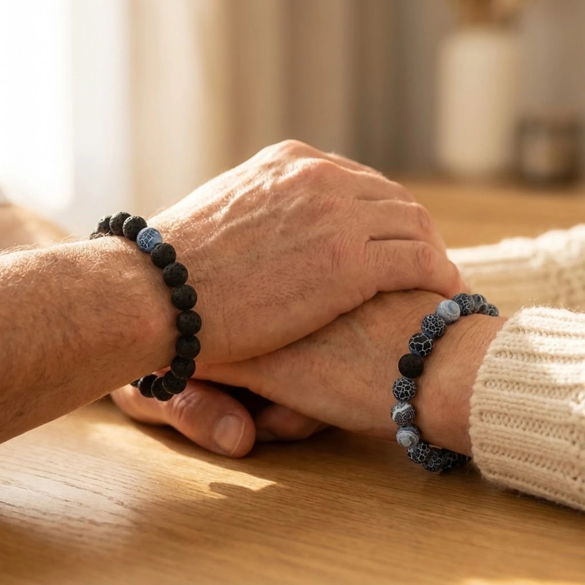 Two hands holding each other on a wooden surface with beaded bracelets.