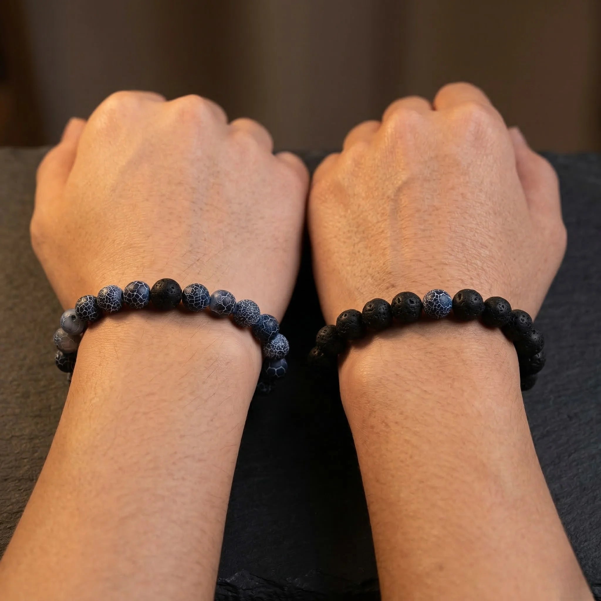 Two wrists wearing black beaded bracelets on a dark background