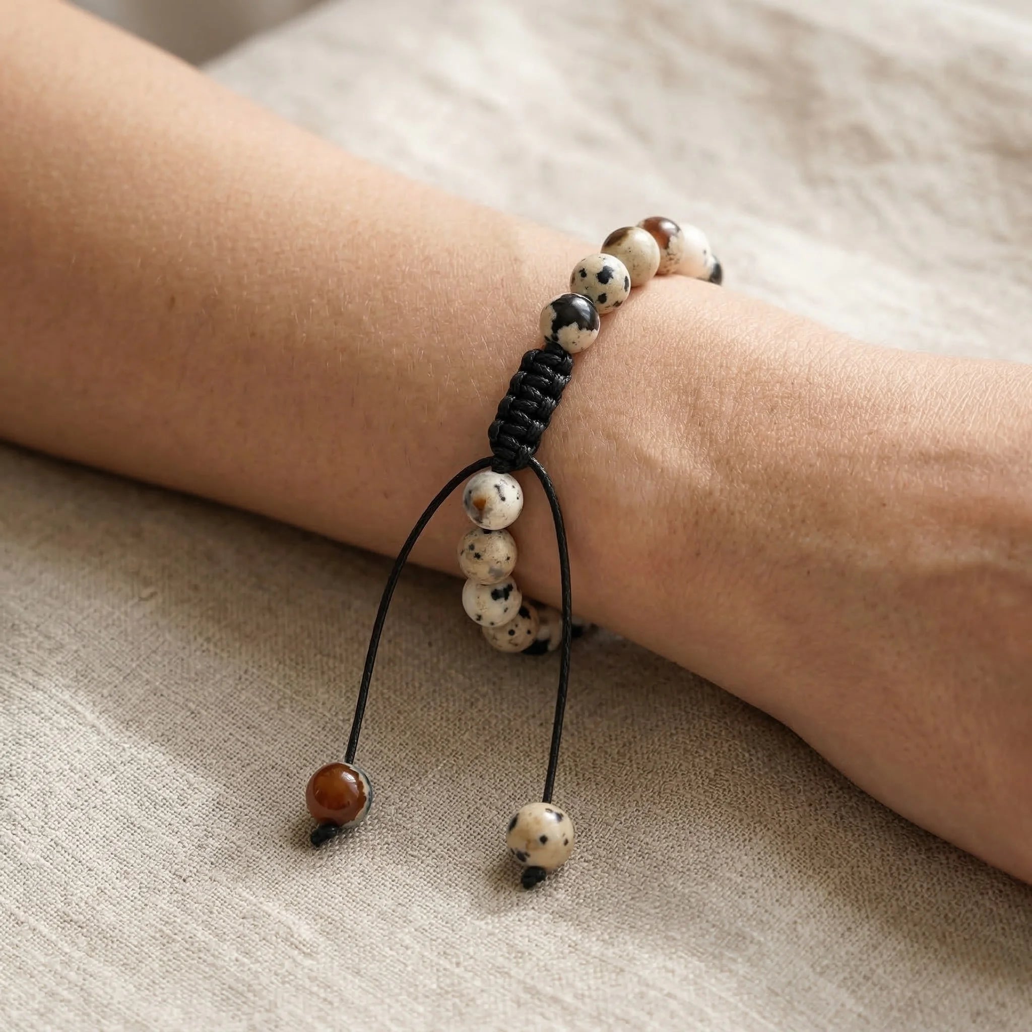 Beaded bracelet with black cord on a wrist against a neutral background