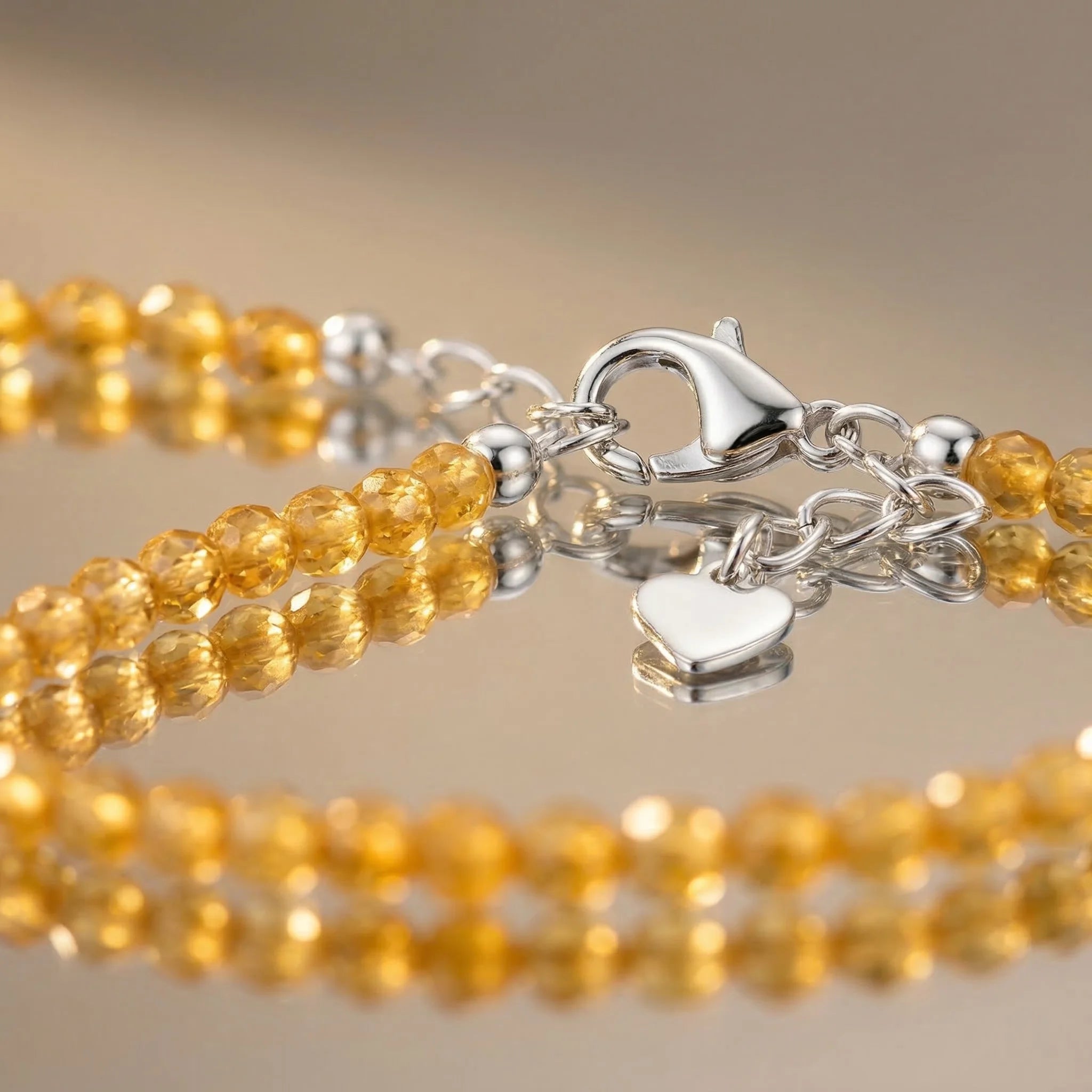 Silver bracelet with a heart charm and yellow beaded bracelets on a beige background