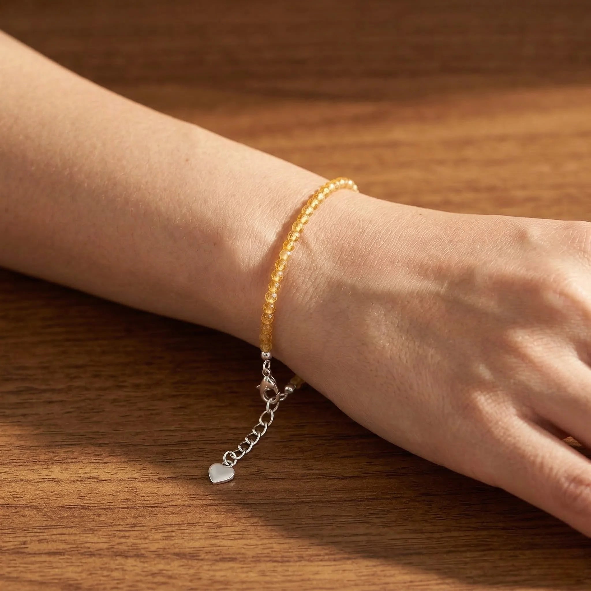 Hand wearing a yellow beaded bracelet with a silver chain on a wooden surface
