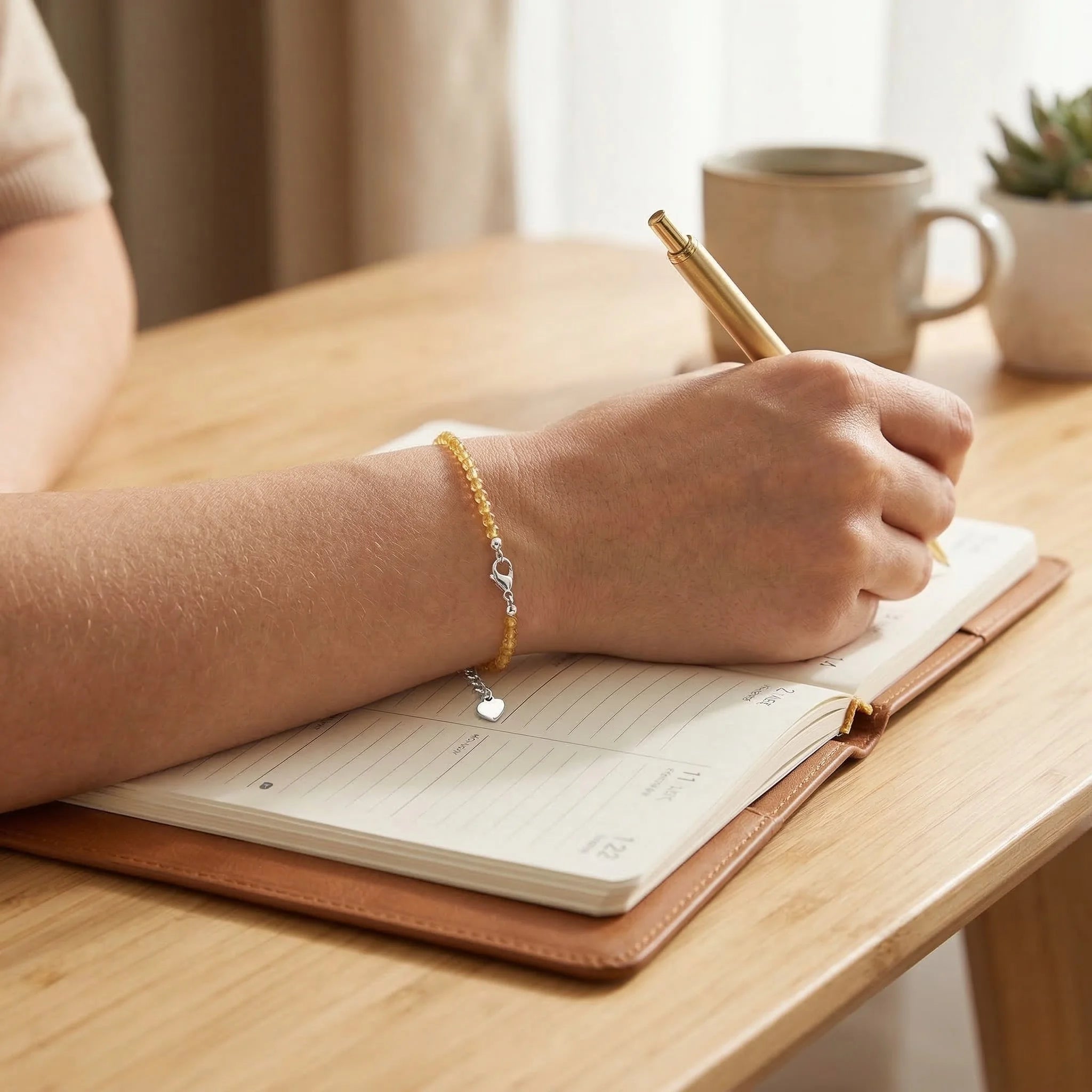 Person writing in a notebook with a pen on a wooden table, wearing a bracelet.