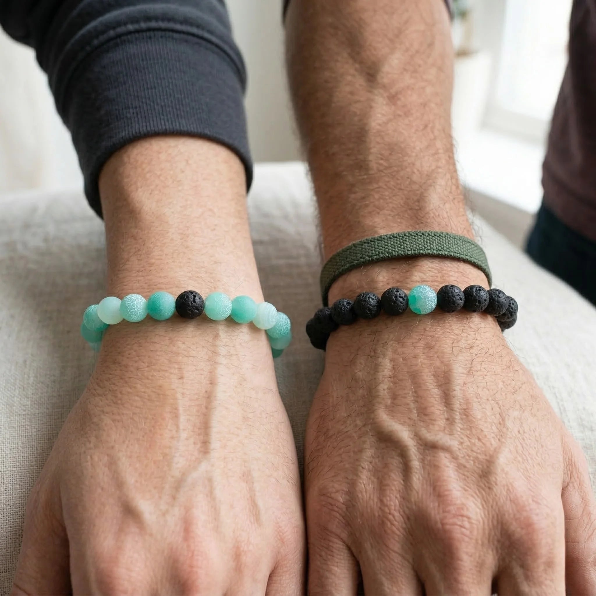 Two hands wearing beaded bracelets on a neutral background