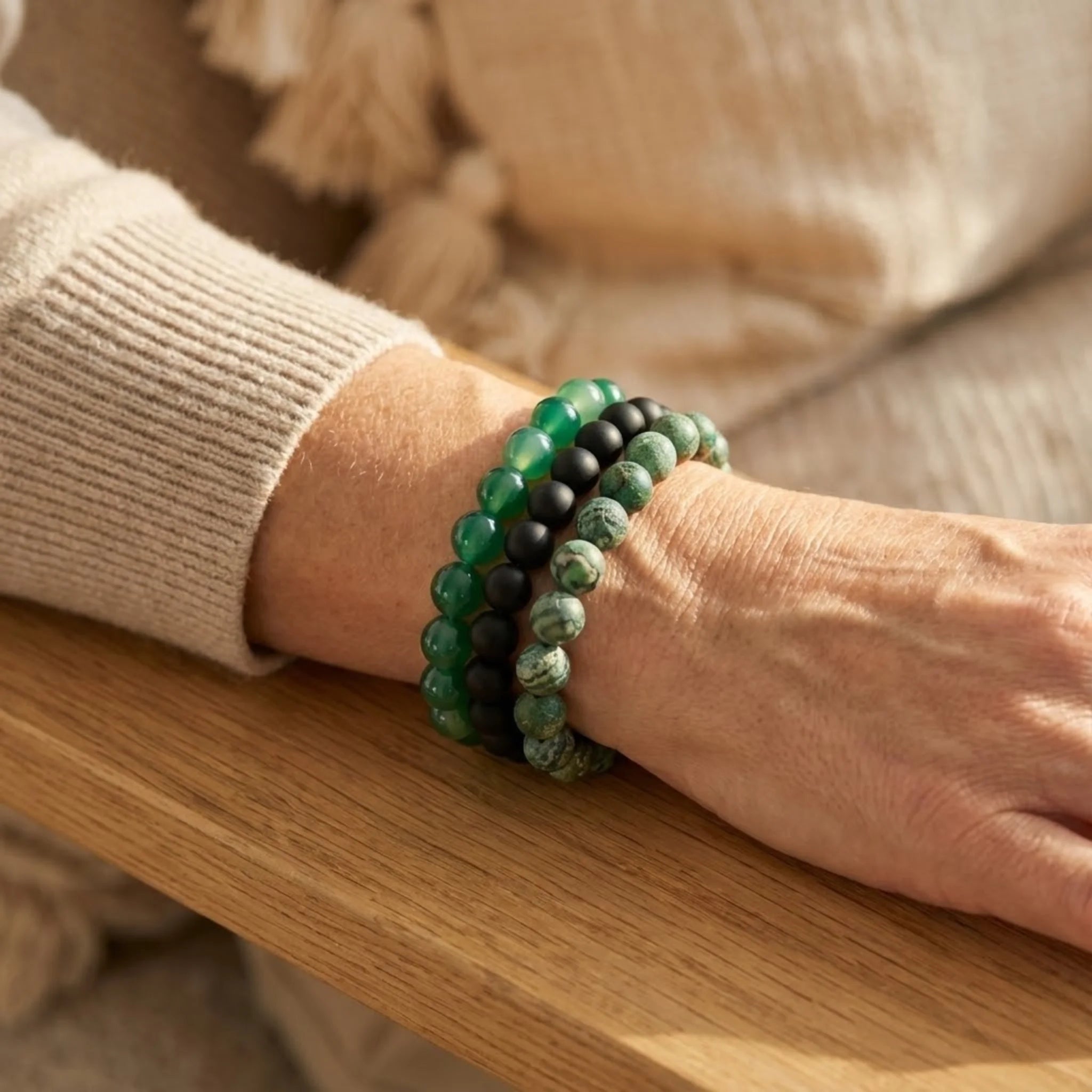 Person wearing two green beaded Harmony intention bracelet stack with green agate, black onyx, and green weathered agate beads for growth and balance bracelets on a wooden surface