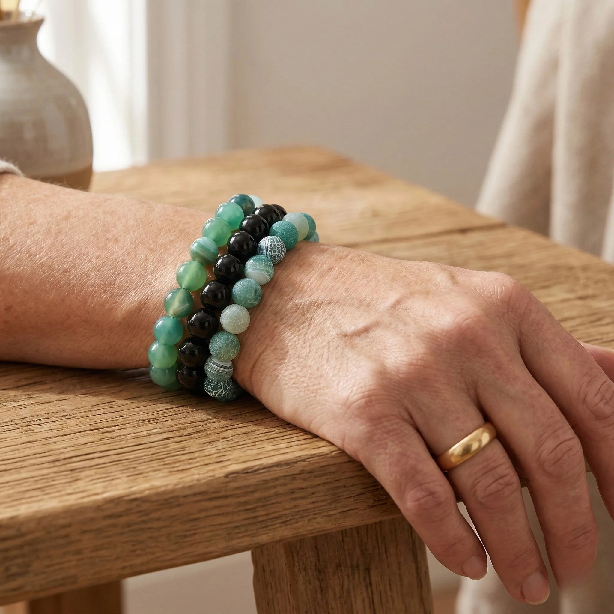 Hand wearing a green beaded bracelet on a wooden surface
