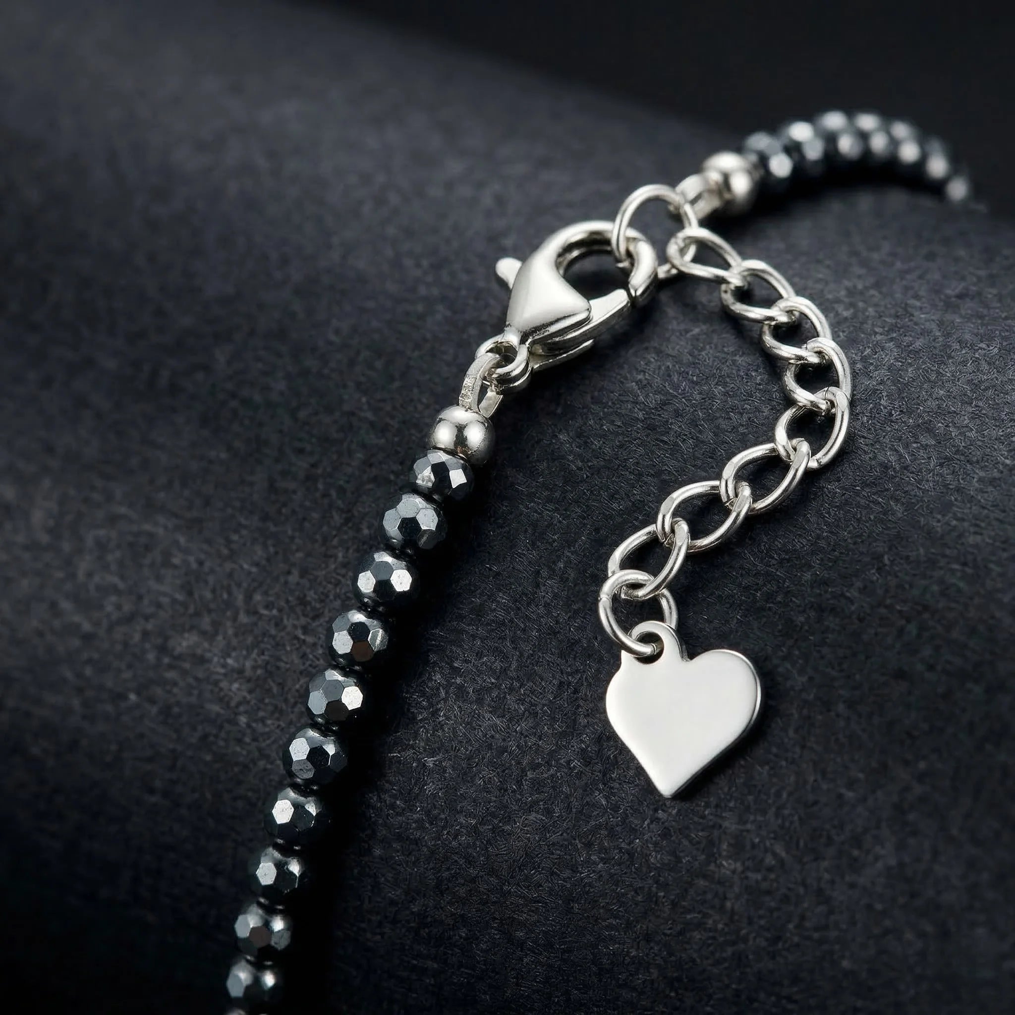 Bracelet with black beads and a silver heart charm on a dark background