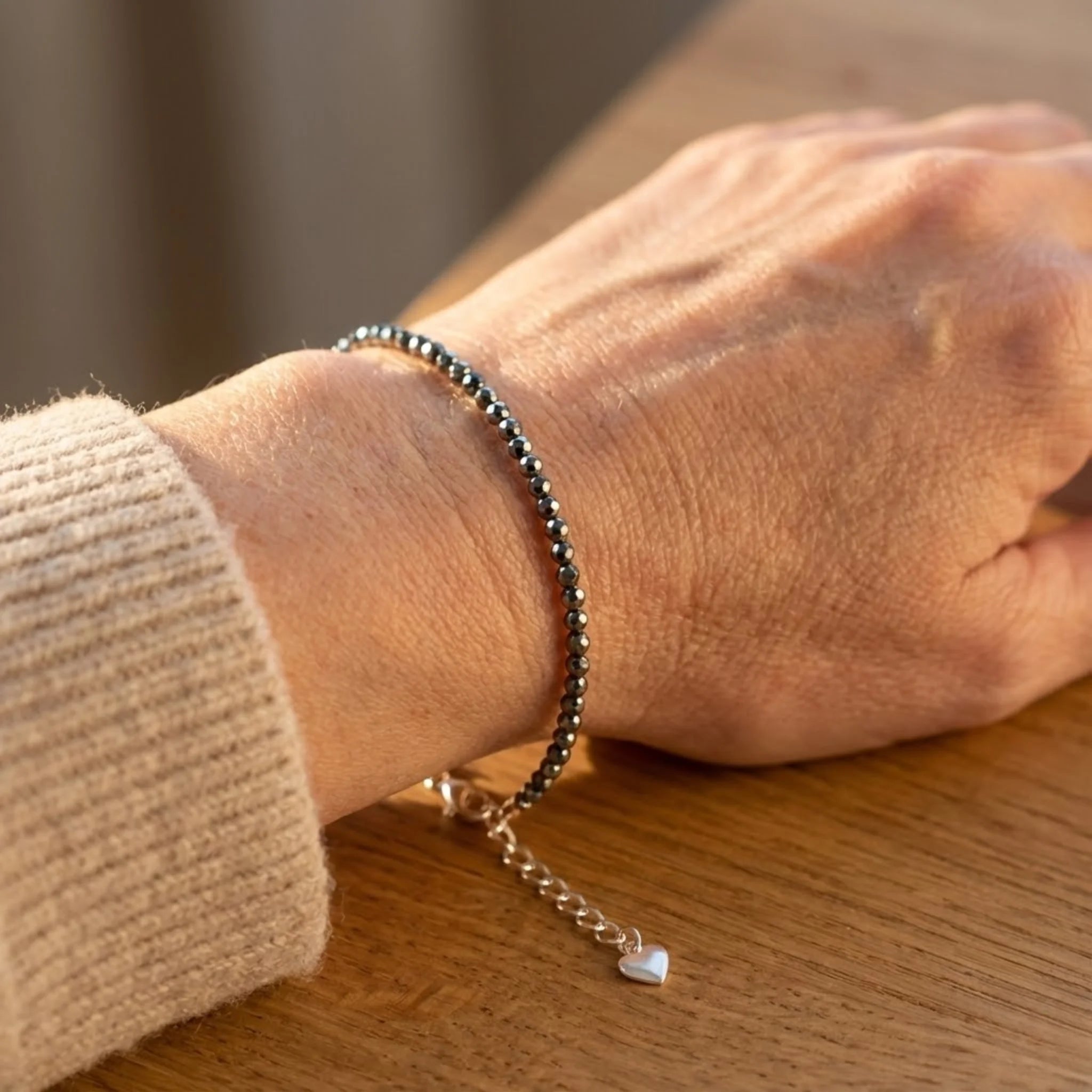 Close-up of a wrist wearing Essential silver bracelet crafted with hematite gemstone beads for a sleek, metallic finish bracelets on a wooden surface