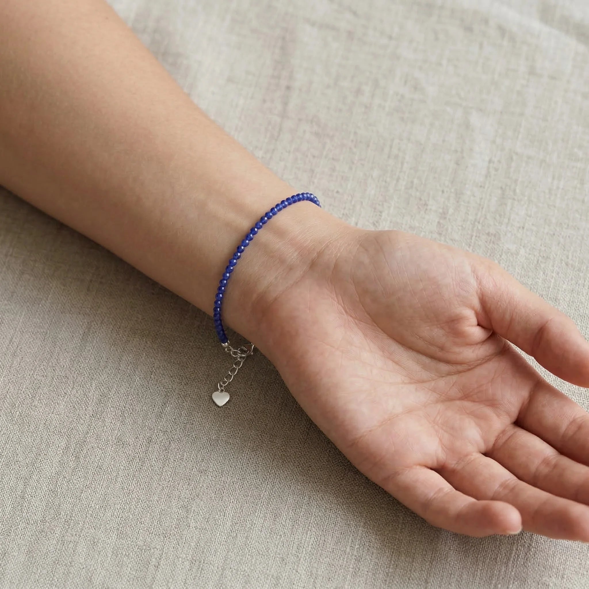 Hand wearing a blue beaded bracelet on a beige fabric background
