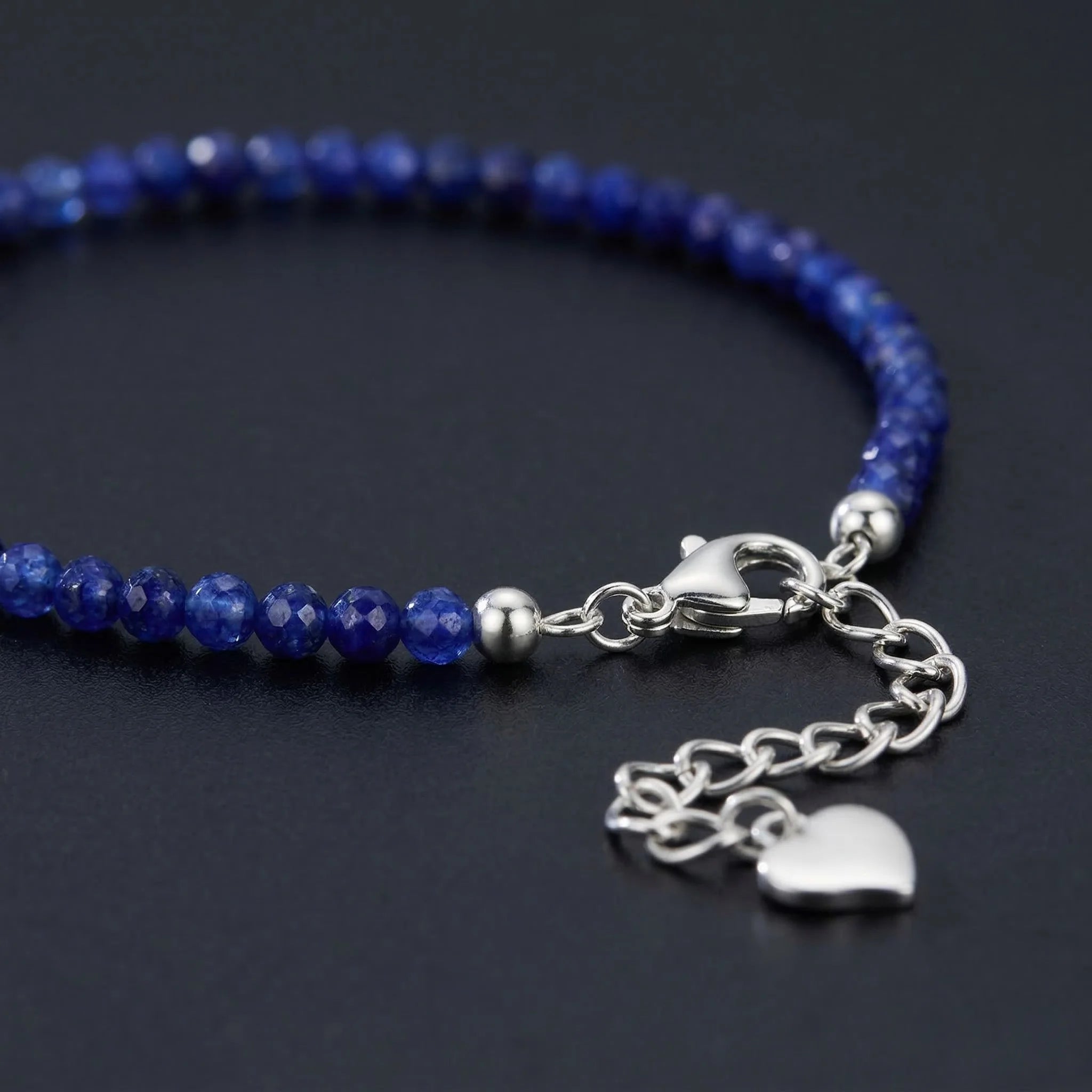 Blue beaded bracelet with silver clasp and heart charm on a dark background