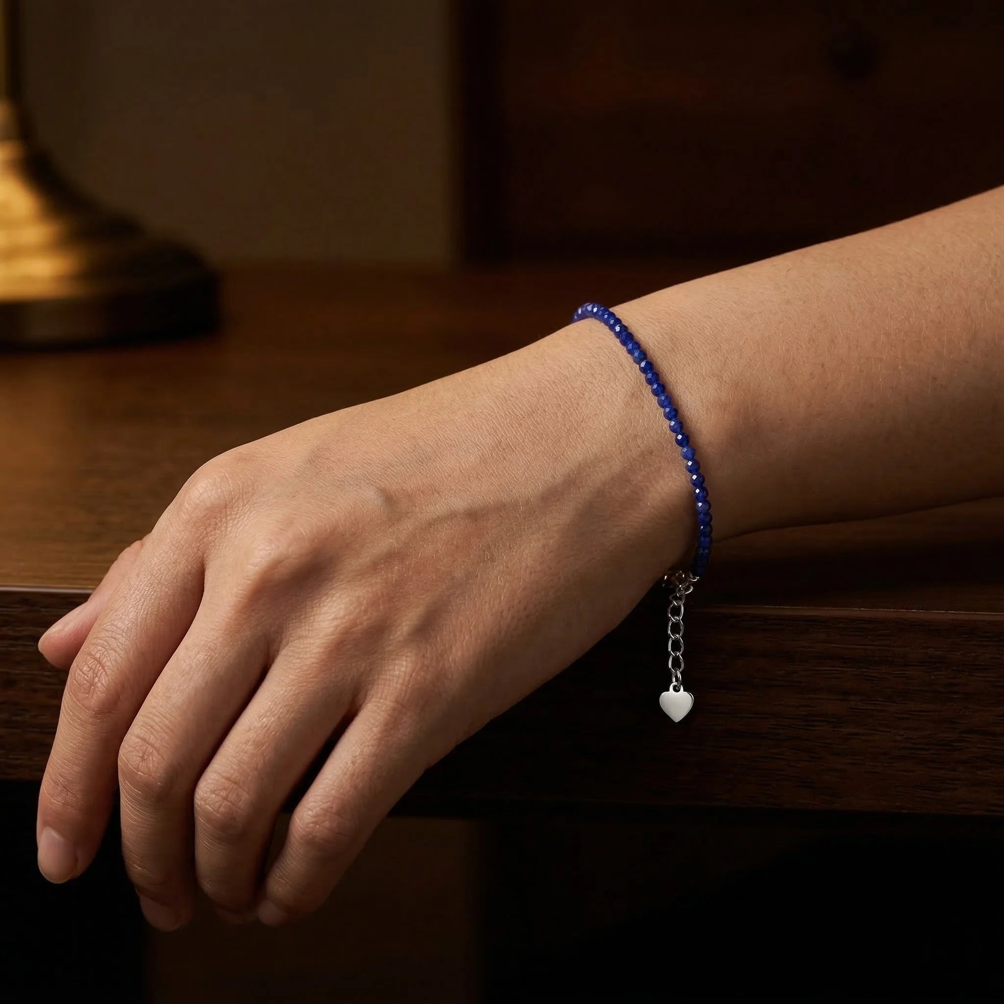 Hand wearing a blue beaded bracelet with a heart charm on a wooden surface
