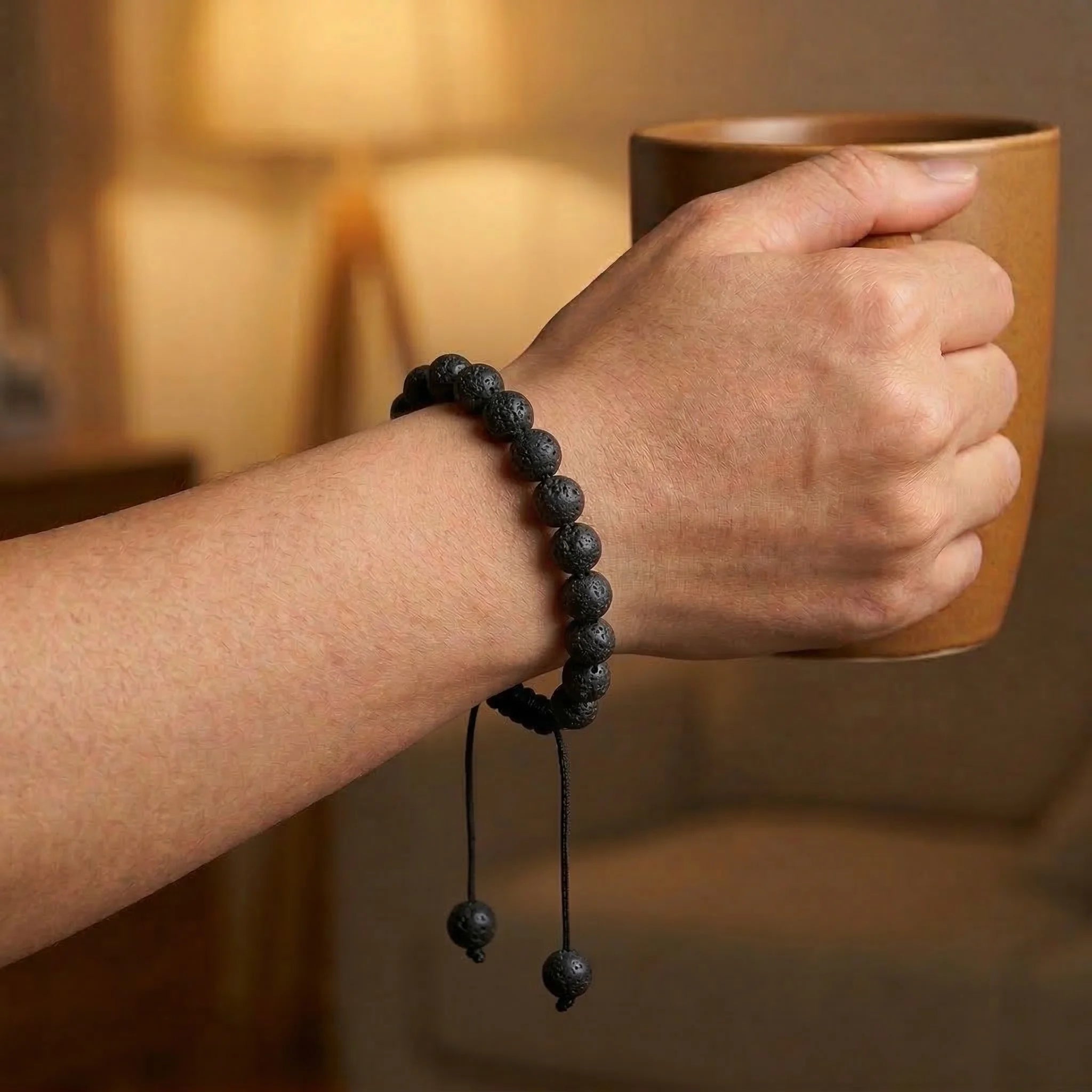 Hand wearing a black beaded bracelet holding a brown mug with a warm background