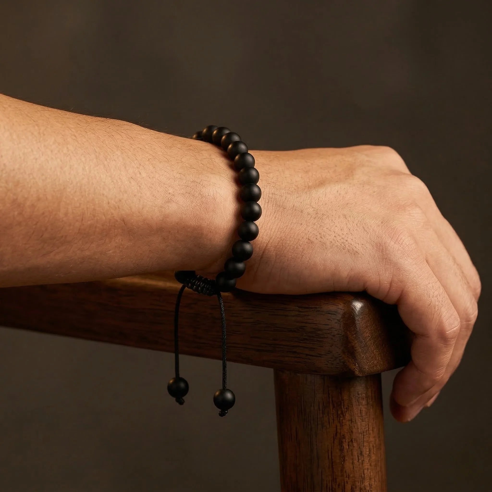 Person wearing a black beaded bracelet on a wooden surface with a dark background