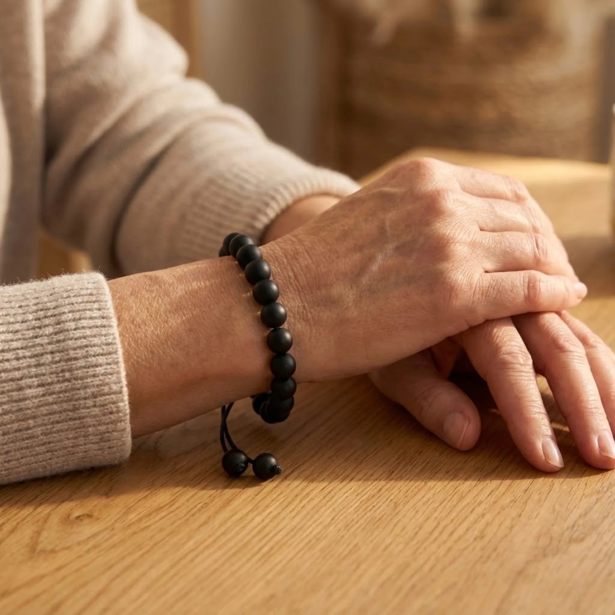 Close-up of a person's hand wearing a black beaded Adjustable balance bracelet made with black onyx beads and braided cord for a clean, modern look bracelet on a wooden surface.